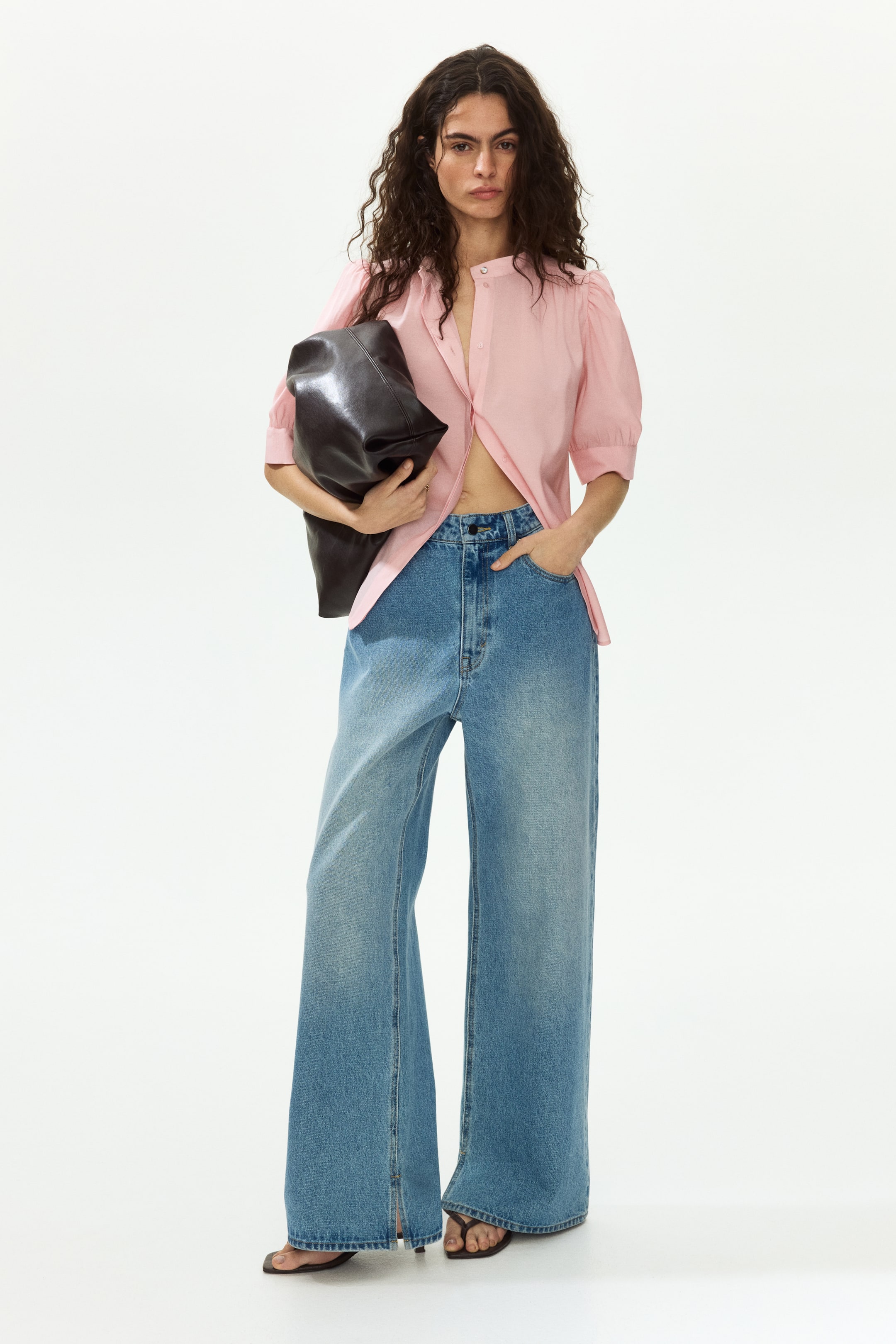 Ampliar la imagen: Una camisa rosa claro con cuello mao presenta mangas cortas abullonadas y un frente parcialmente desabotonado, mientras que los jeans azul claro de tiro alto y pierna ancha muestran dobladillos divididos en los tobillos.