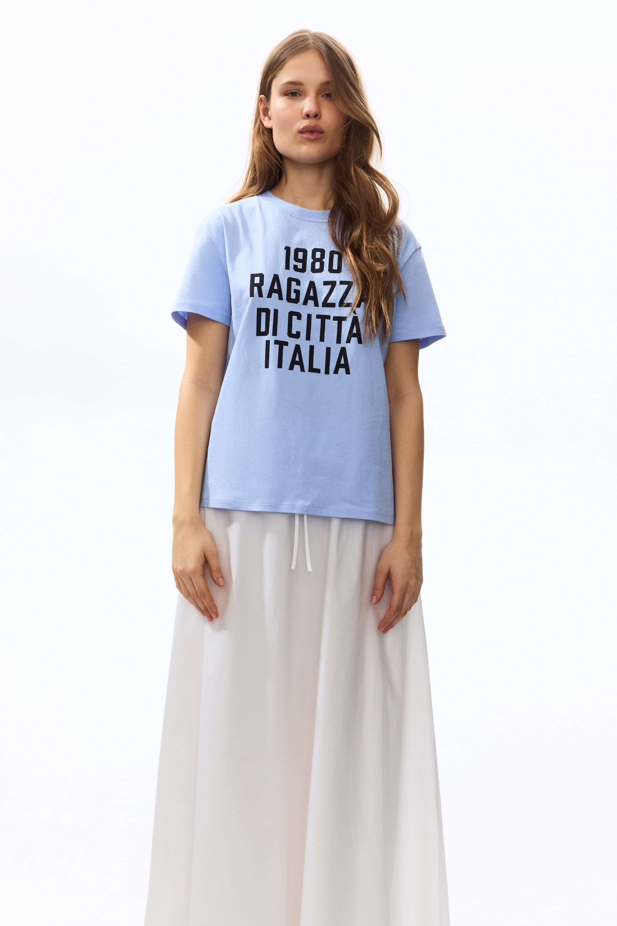 View larger image: The light blue short-sleeve t-shirt features a crew neck and bold black text, "1980 RAGAZZA DI CITTÀ ITALIA," across the front. It offers a relaxed fit when viewed from the front.