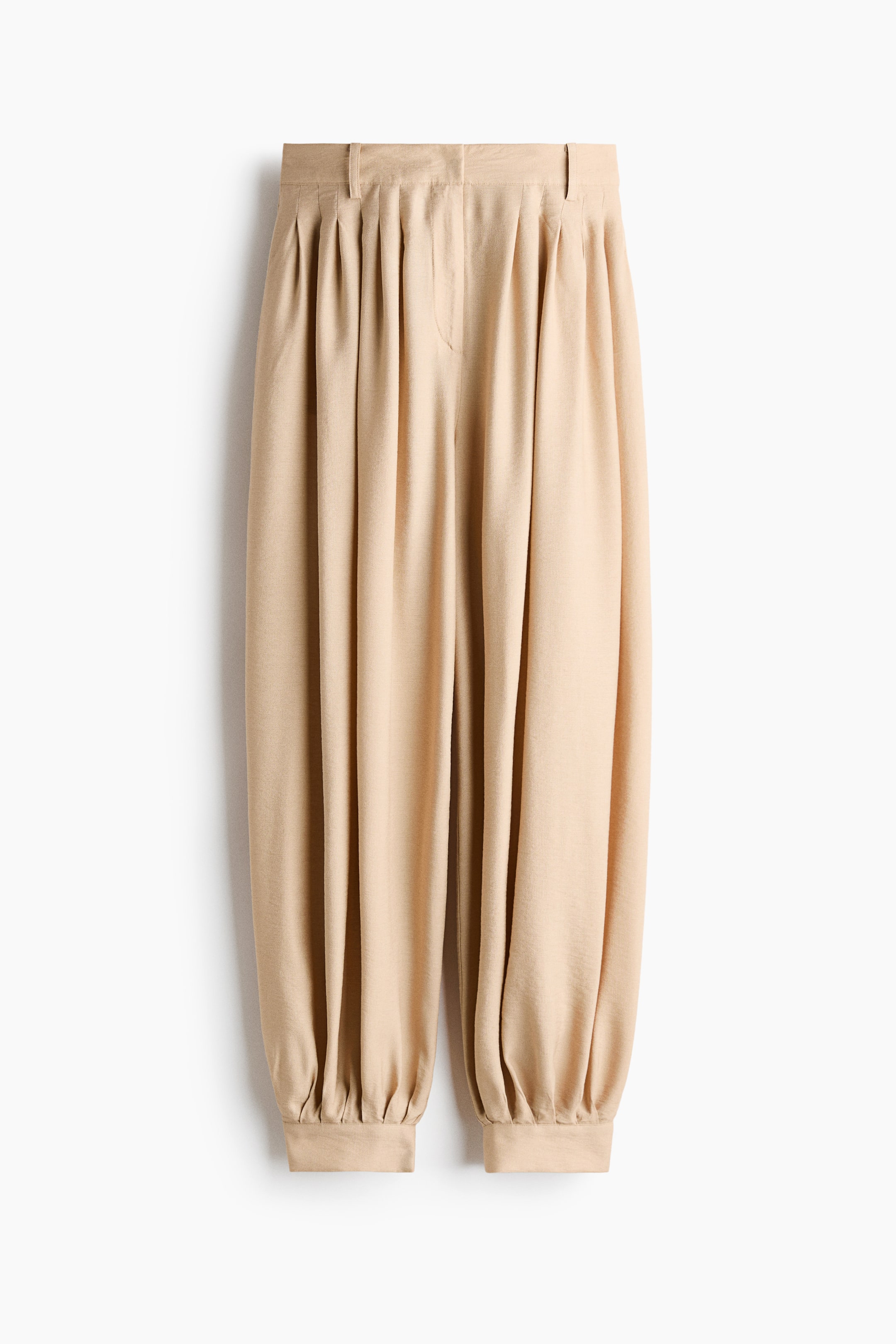 Agrandir l'image: Un pantalon beige est présenté de face, avec une ceinture plate dotée de passants, plusieurs plis sous la taille et des poignets élastiqués.