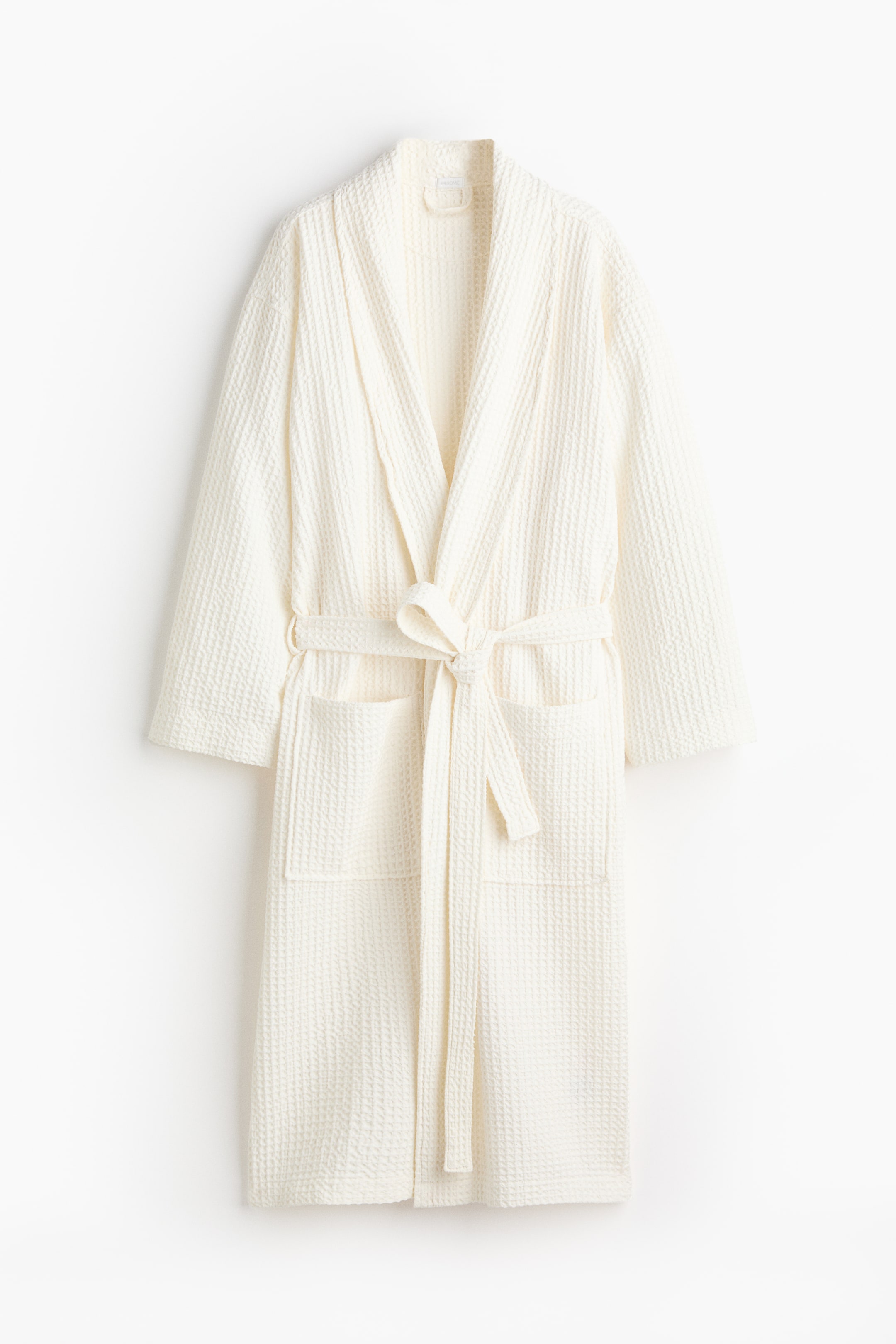 View larger image: A cream dressing gown is facing FRONT, displaying its waffle-weave cotton fabric. It is featuring a shawl collar, two patch front pockets, and a tie belt tied at the waist.