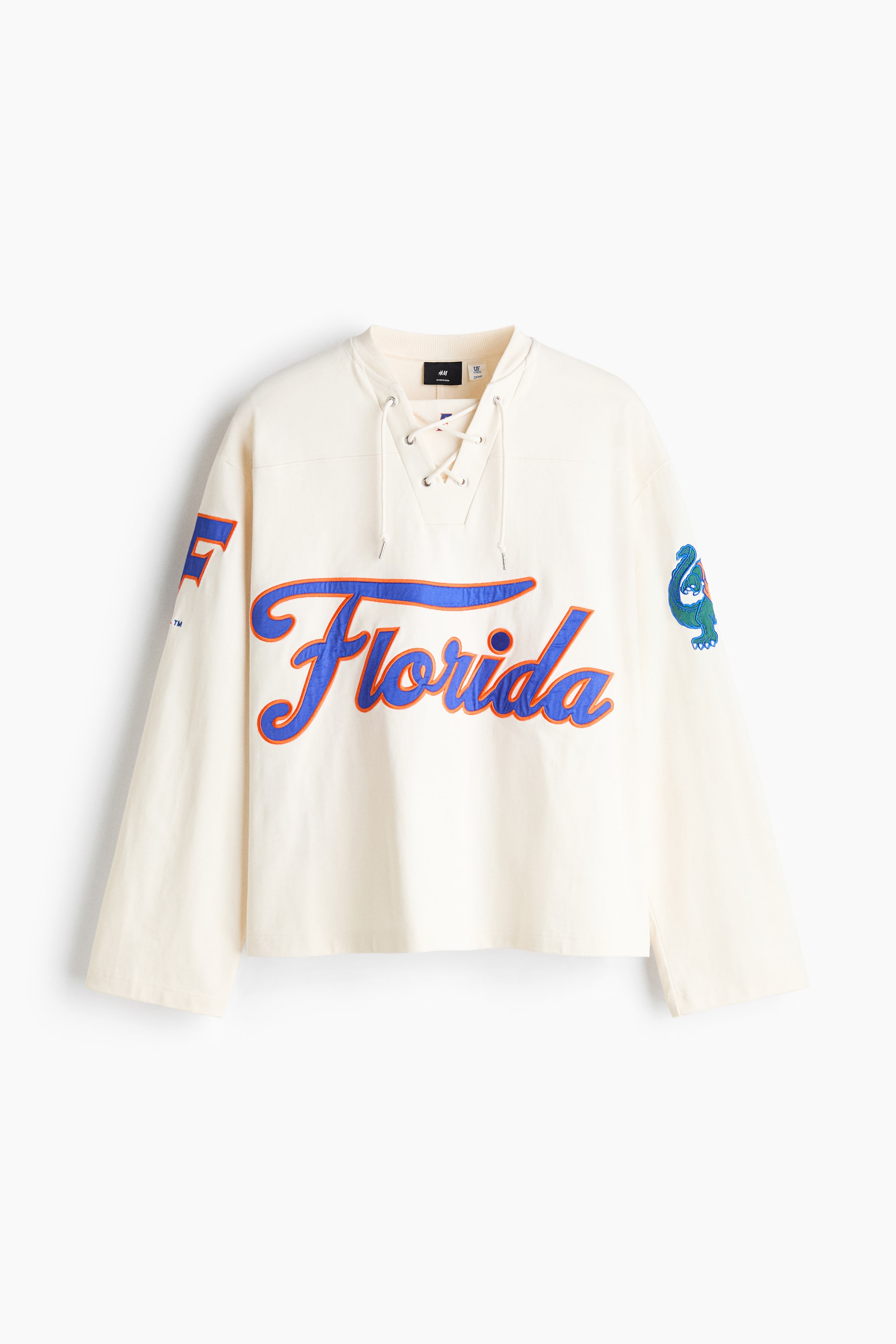 View larger image: An off-white, oversized long-sleeved T-shirt is shown from a front-facing angle, featuring a lace-up V-neckline with a fabric insert and dropped shoulders. A large blue "Florida" script graphic with an orange outline is displayed across the chest, with additional collegiate motifs decorating the wide sleeves.