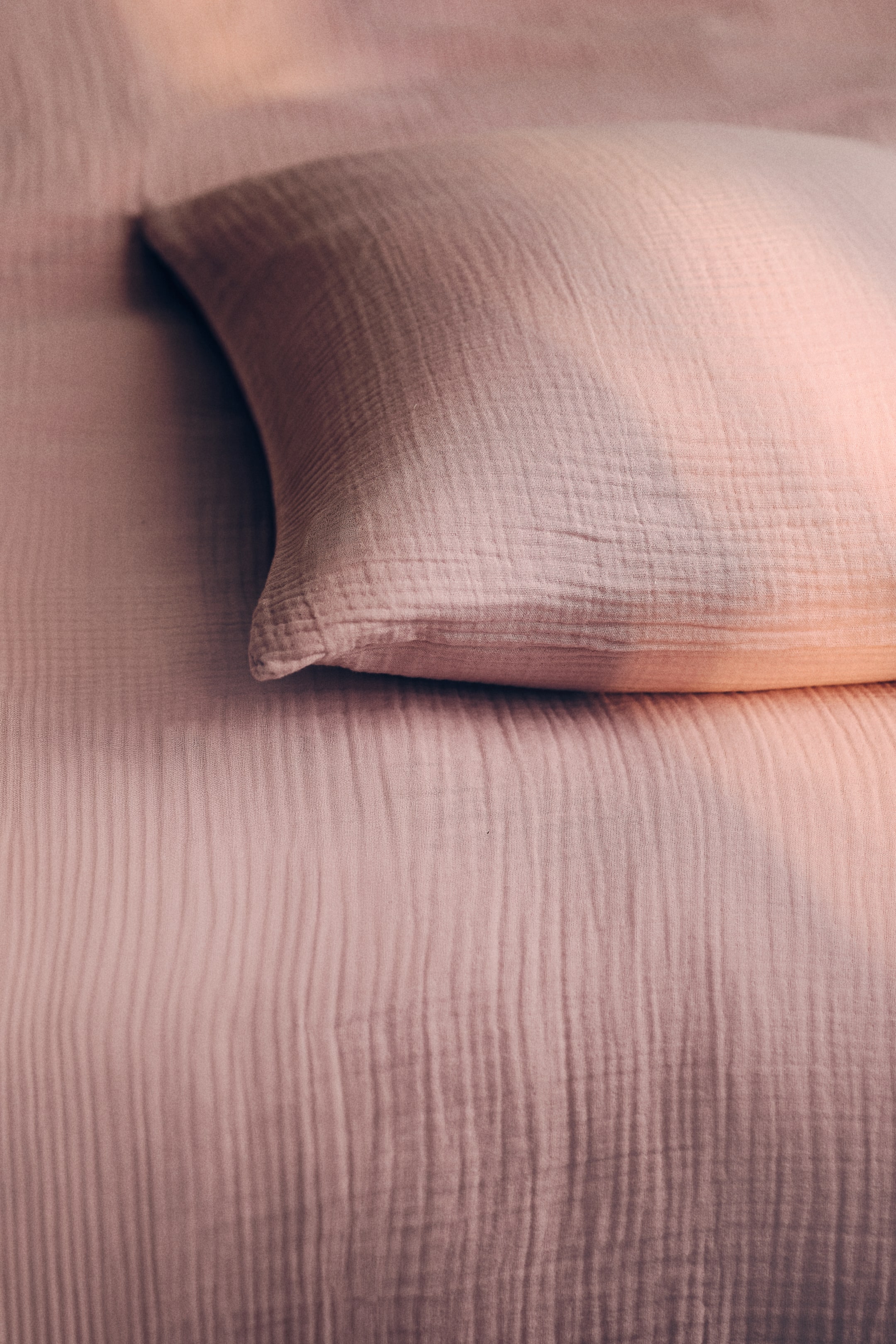 Agrandir l'image: Un ensemble de housse de couette simple présente un tissu en mousseline de coton froissé rose clair. Une taie d'oreiller assortie est partiellement visible, reposant sur la housse de couette.