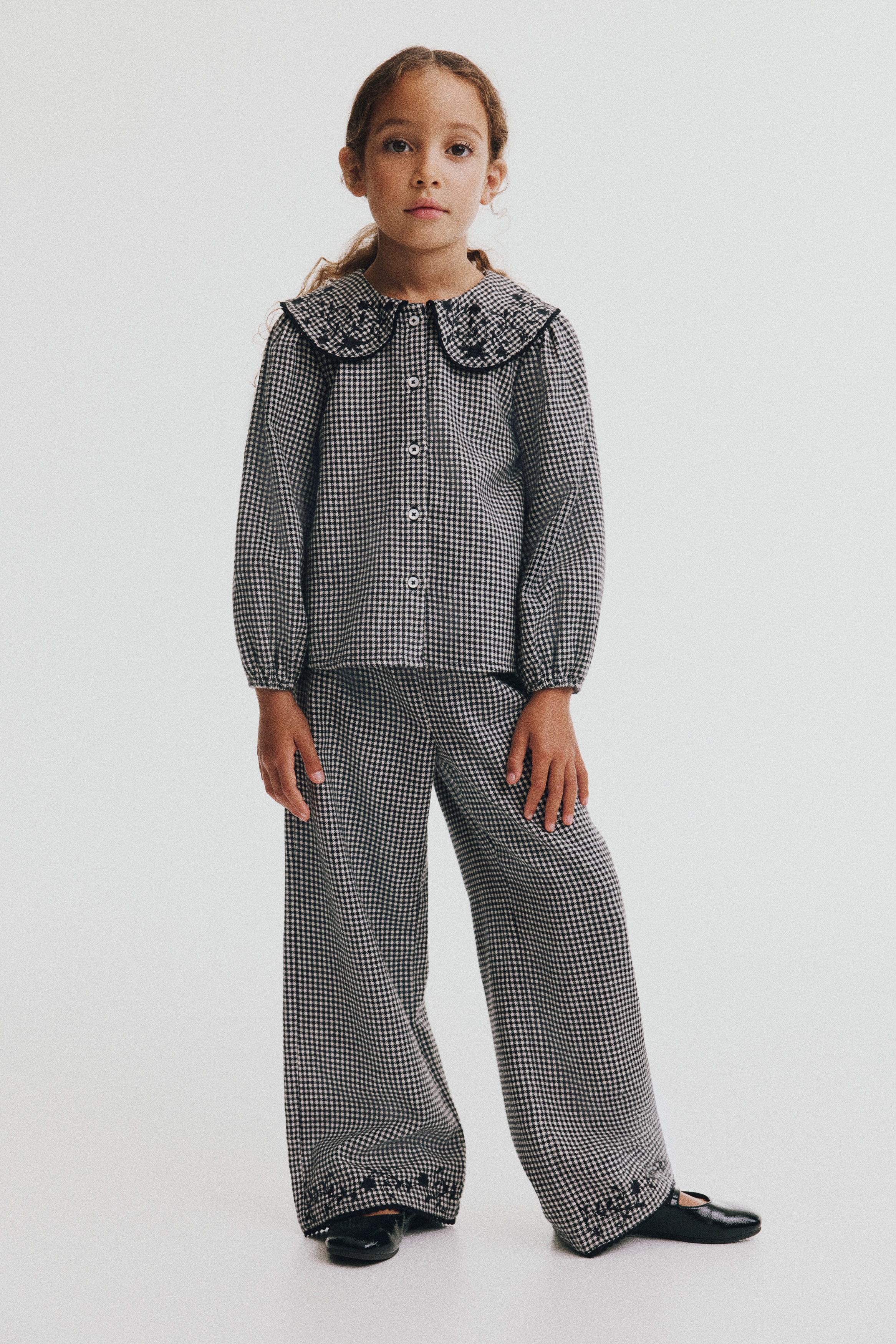 Ove pantalone od pamuÄnog kepera sa crno-belim Å¡arom âhoundstoothâ prikazane su sprijeda, sa nabranim elastiÄnim pojasom i ravnim nogavicama. Donji porubi ukraÅ¡eni su crnim cvetnim vezom i zavrÅ¡eni delikatnom crnom picot trakom.