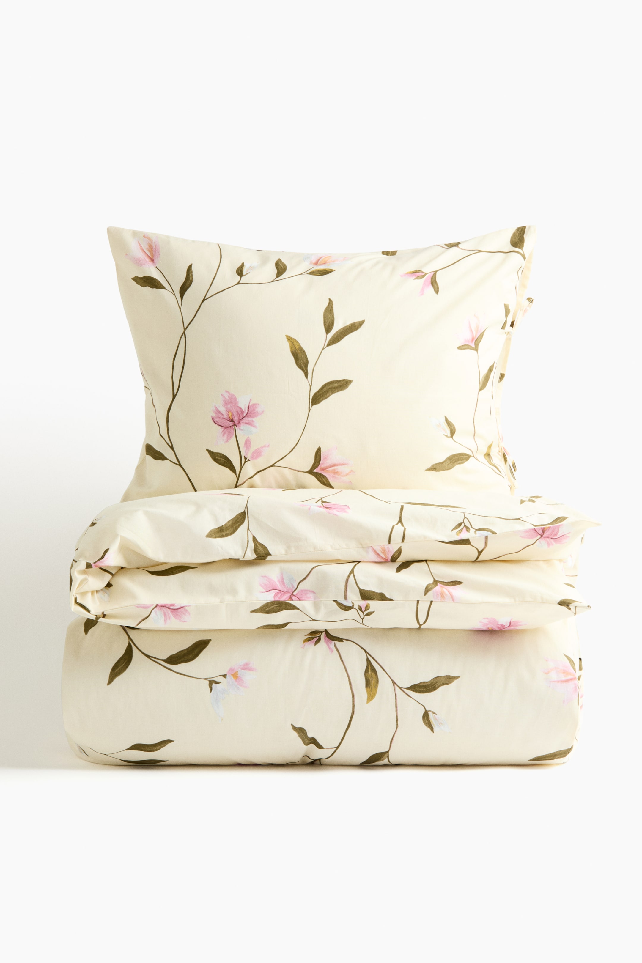 View larger image: A creamy yellow bedding set is displaying a floral pattern with brown stems, green leaves, and pink and white flowers. The front of a pillowcase is standing upright, and a duvet cover is folded neatly beneath it.