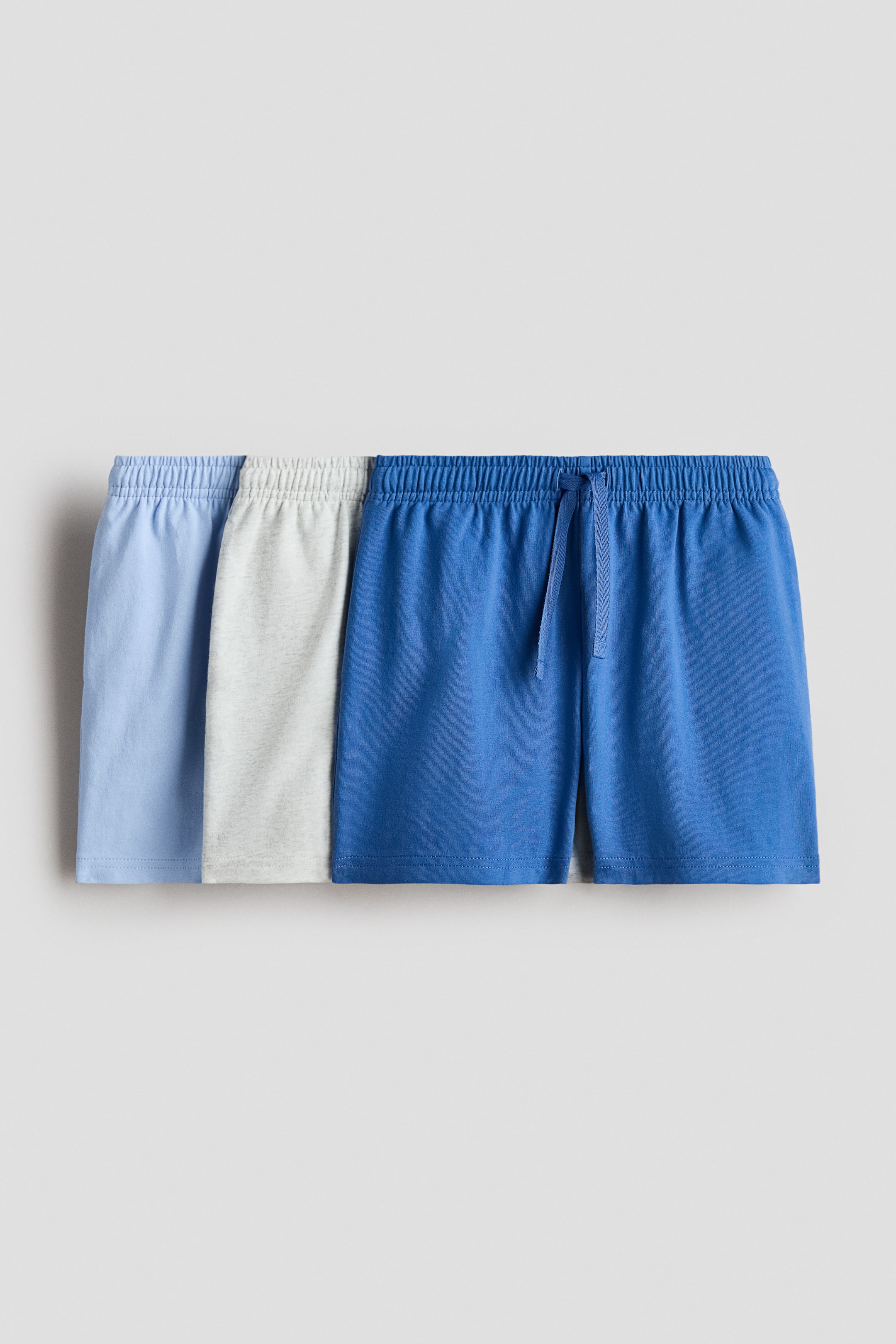 View larger image: Three pairs of soft cotton jersey shorts are on display, facing front, in light blue, light grey, and royal blue hues. Each pair features an elasticated waistband, with the royal blue pair additionally showcasing a visible drawstring tie at the center front.