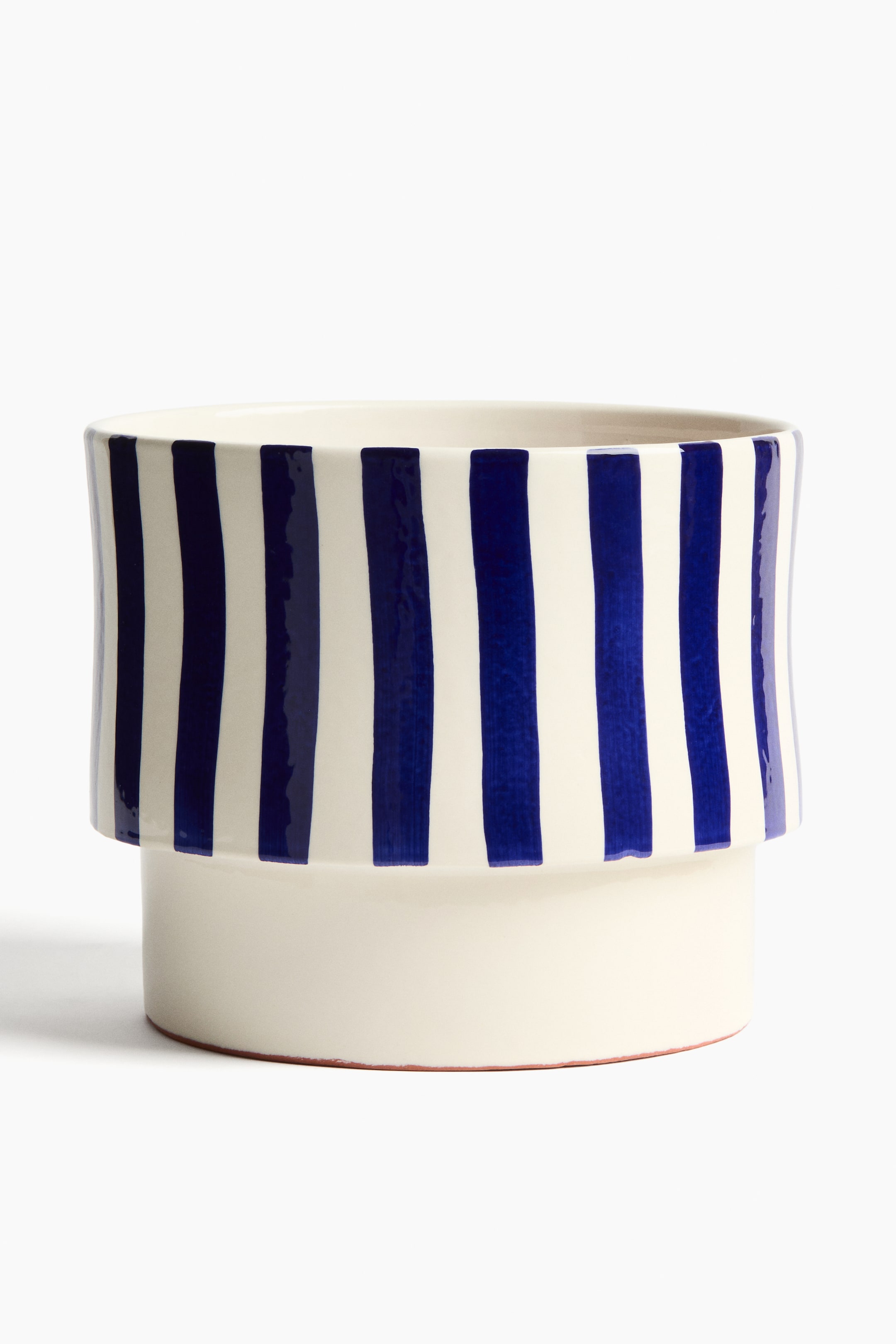 Visualizza immagine più grande: Un vaso per piante in terracotta smaltata extra-large è presentato frontalmente, caratterizzato da un design a gradini. Il vaso è bianco, con strisce verticali irregolari di colore blu scuro che decorano la sua sezione superiore più ampia, mentre la sezione inferiore più stretta è di un bianco solido, e un bordo non smaltato di colore marrone rossastro è visibile alla base.