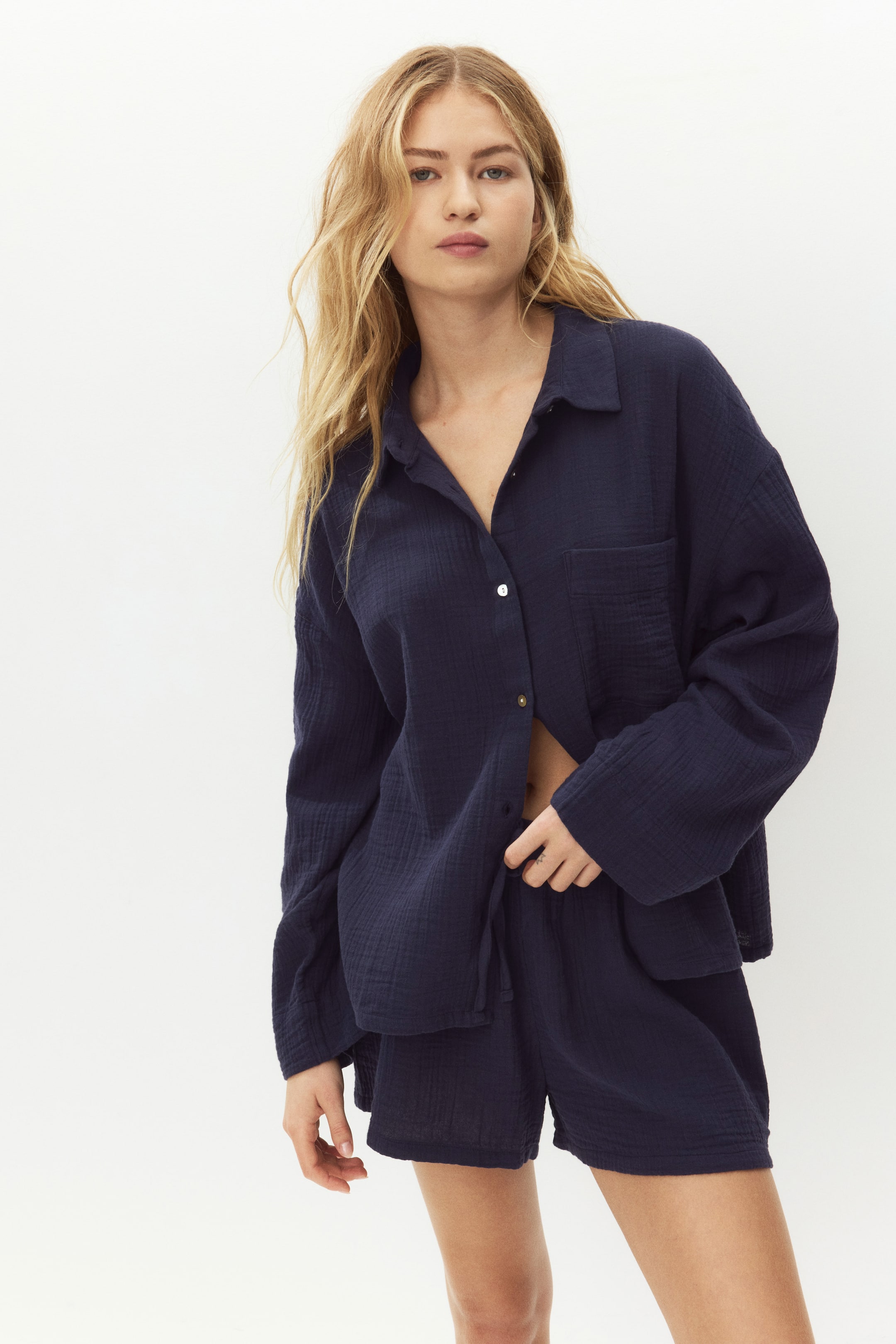 View larger image: A navy blue two-piece set featuring a long-sleeved, collared shirt with a partially unbuttoned front and a chest patch pocket, complemented by matching pull-on shorts with a drawstring waist. The set offers a relaxed fit and a textured, crinkled fabric.