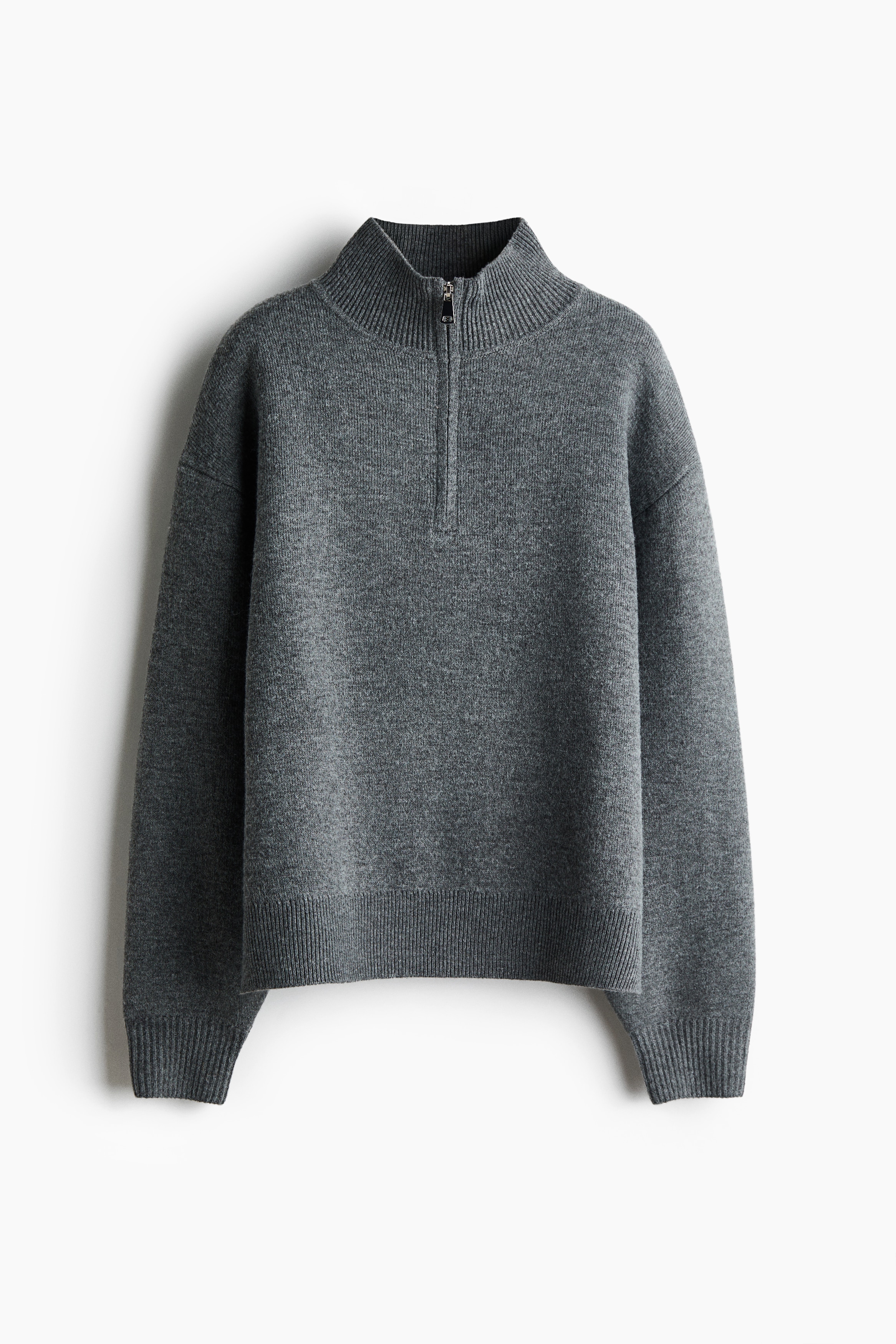 The model is wearing an oversized grey fine-knit jumper, featuring a high collar with an open silver half-zip. The jumper is designed with dropped shoulders, long sleeves and a ribbed hem.