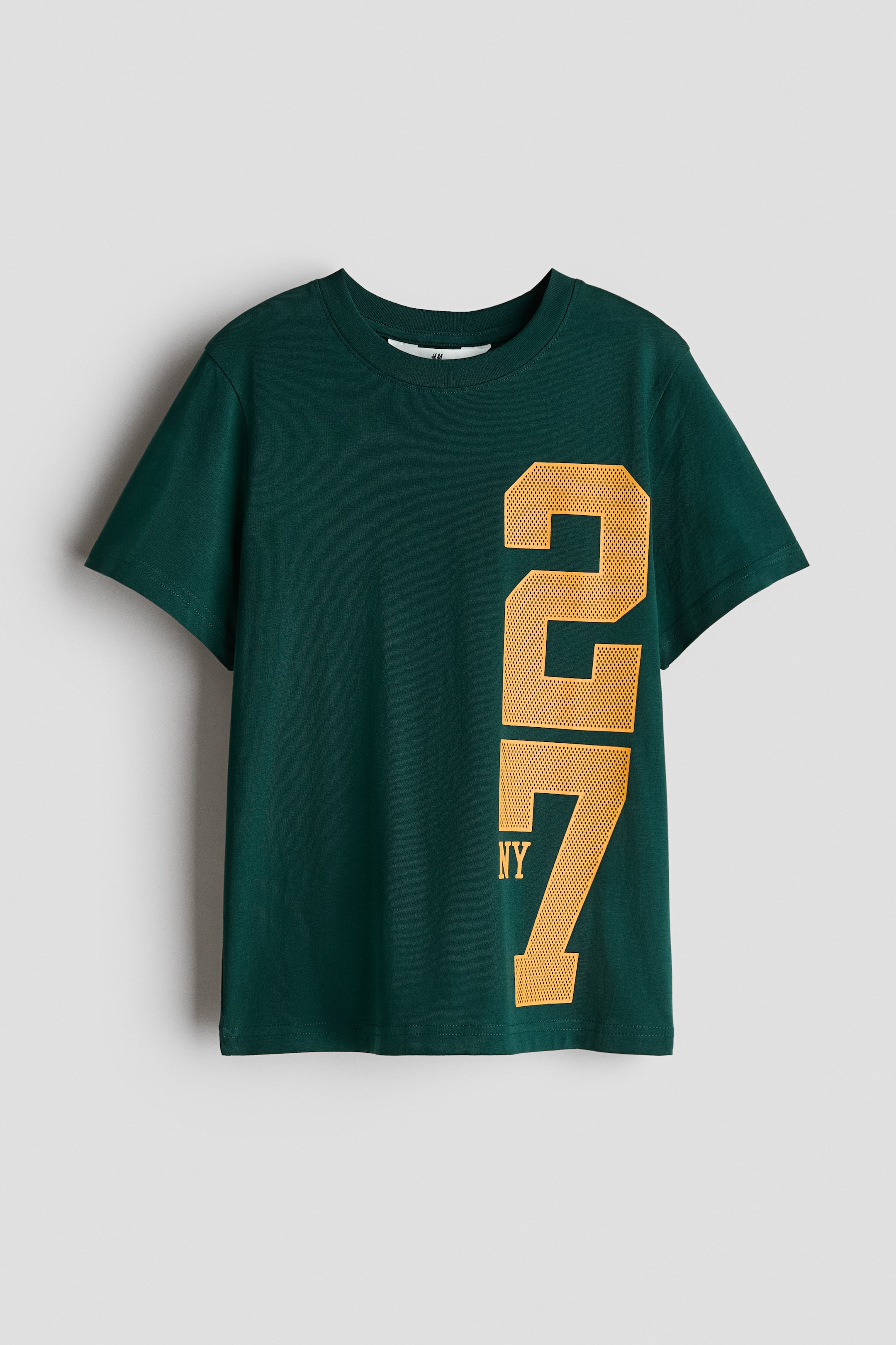 拡大画像を表示: 柔らかいダークグリーンのコットンジャージー素材で作られたクラシックなTシャツには、リブ付きのラウンドネックラインが特徴です。フロントには、右側にメッシュテクスチャーのイエローで縦に大きく「27」とプリントされ、その下に「NY」がプリントされています。