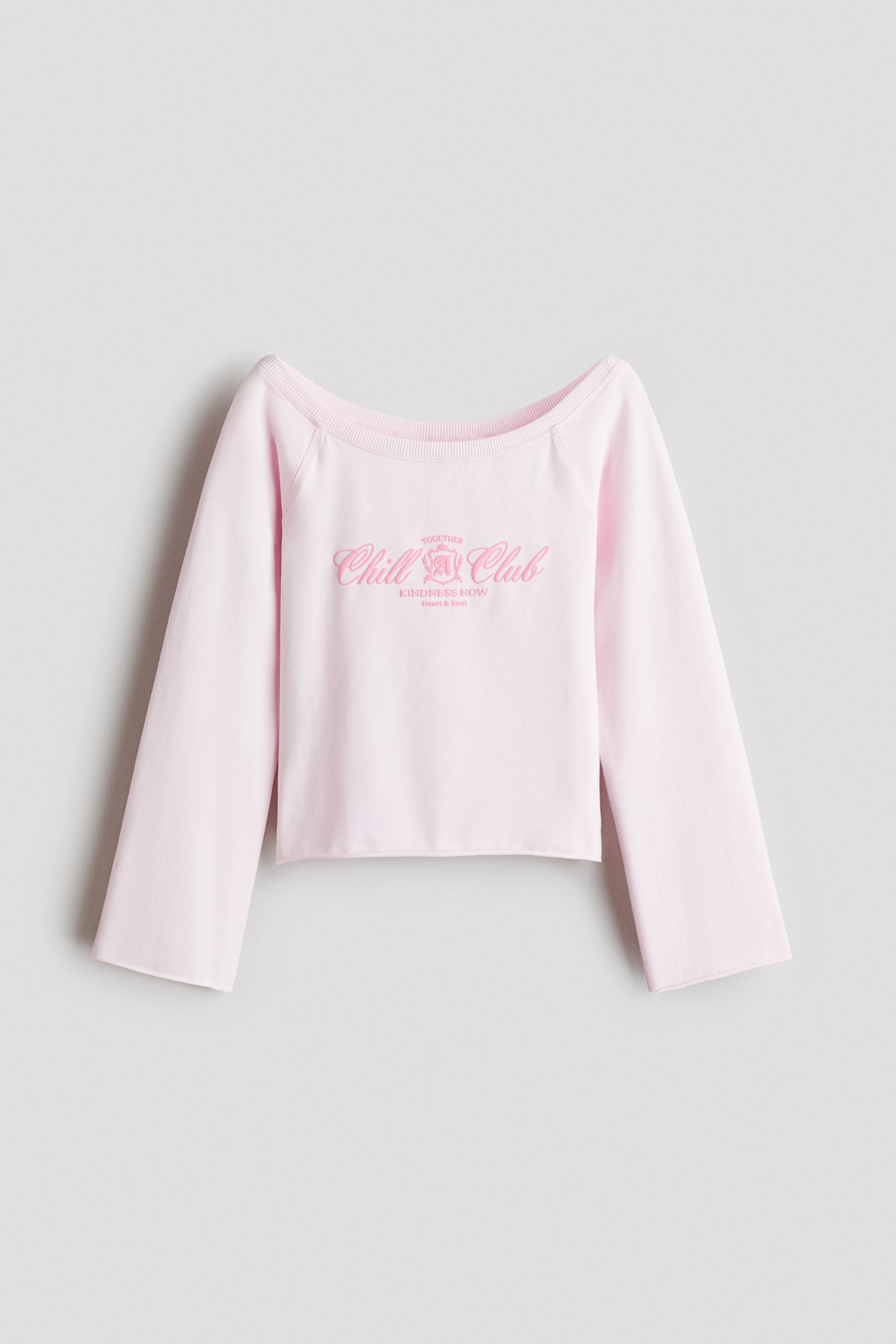 View larger image: This front view shows a light pink sweatshirt top featuring a wide, rib-trimmed boat neckline and wide raglan sleeves. The chest features a pink text print that reads "Chill Club," while the cuffs and hem feature raw, rolled-up edges.