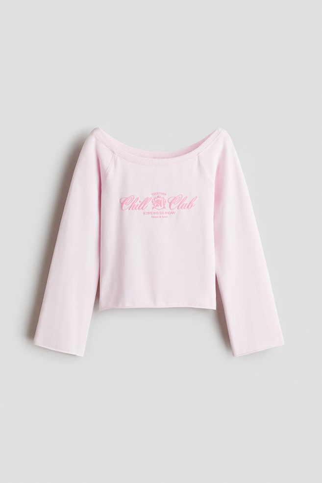 Esta vista frontal muestra una sudadera de color rosa claro con un amplio escote barco rematado en canalé y mangas raglán anchas. En el pecho se ve un estampado de texto rosa que dice "Chill Club", mientras que los puños y el bajo presentan bordes sin rematar y vuelta. - 1