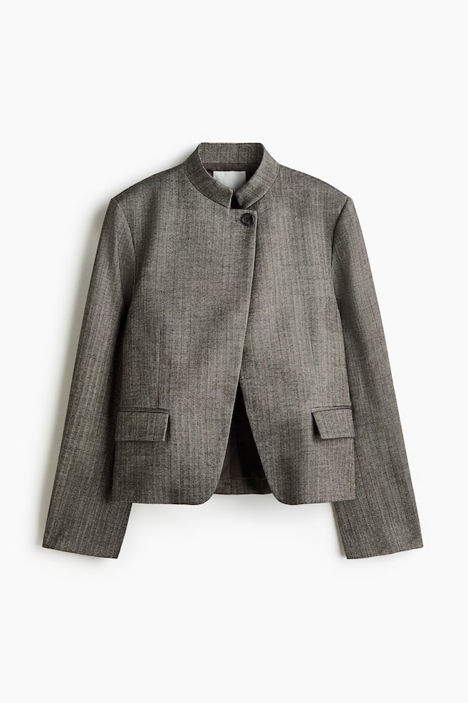 A single-breasted blazer in a gray-brown woven fabric is shown from the front, featuring a stand collar, a lapelless neckline, and a single-button closure at the top. The boxy, oversized-fit blazer is styled with padded shoulders, front waist darts, and two jetted pockets with flaps. - 1