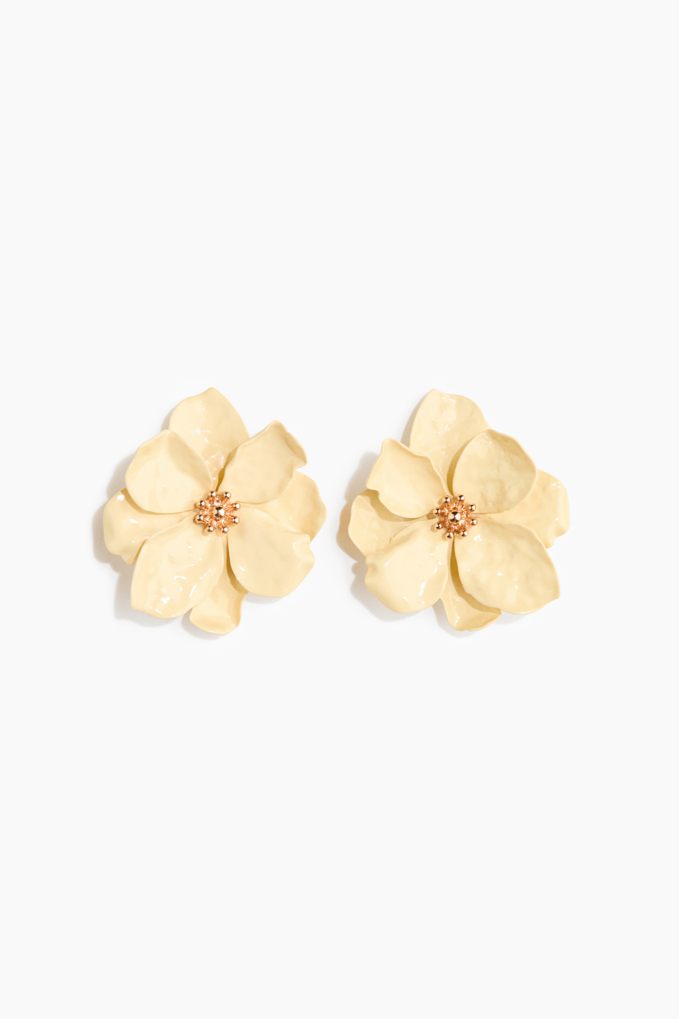 View larger image: A pair of large, flower-shaped stud earrings are on display from the front, each adorned with delicately crafted cream-hued metal petals. The center of each earring features a rose gold-toned, textured design.