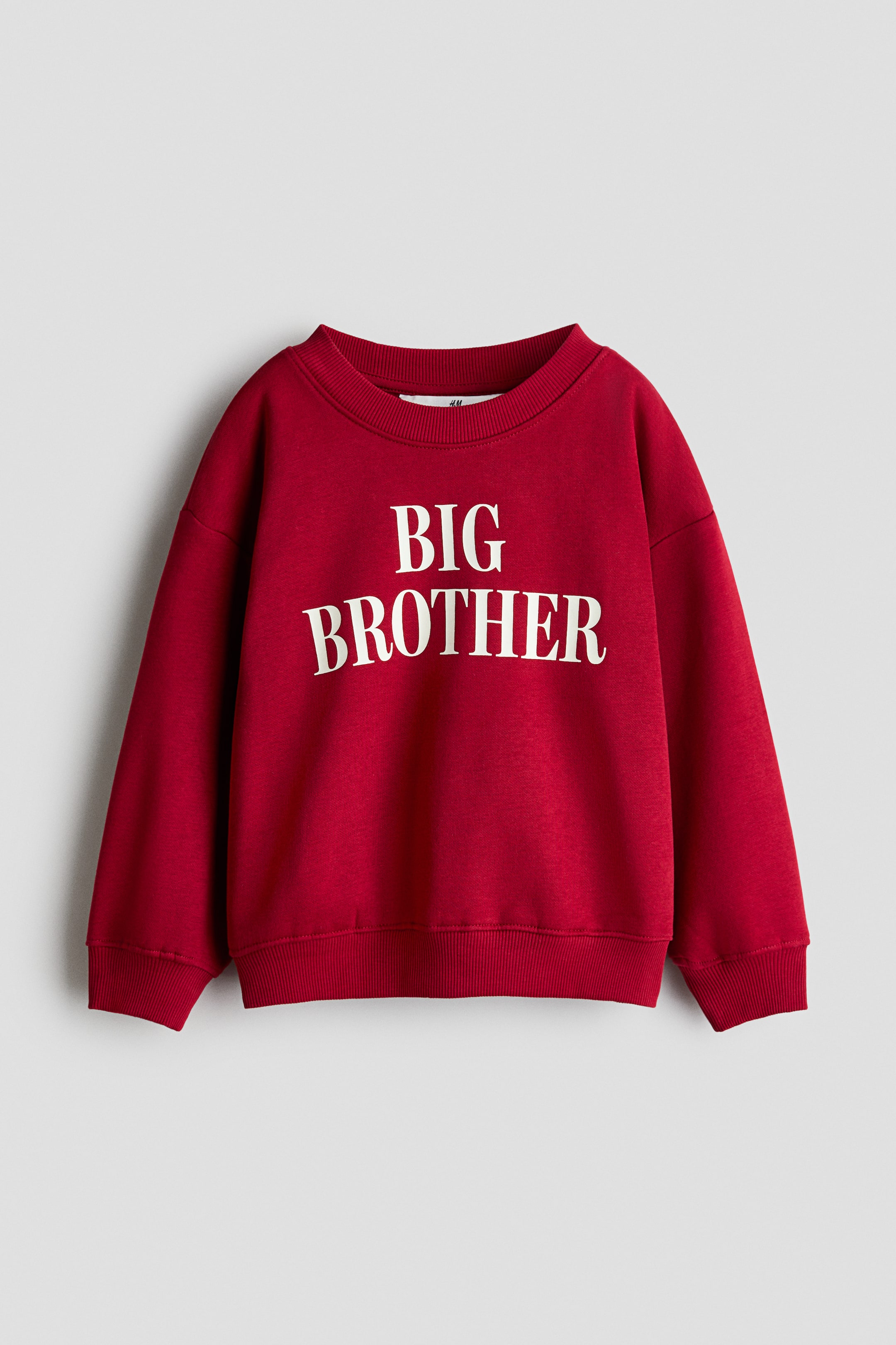 查看大圖: 一件紅色寬鬆版型毛衣正面展示,胸前印有白色「BIG BROTHER」字樣。該服飾呈現圓領羅紋領口、落肩設計,以及袖口與下擺的羅紋細節。