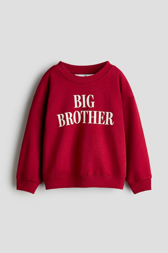 En rød løstsiddende sweater er vist forfra og har et hvidt "BIG BROTHER"-print på brystet. Plagget er designet med en rund, ribkantet halsudskæring, sænkede skuldre samt ribdetaljer ved manchetterne og sømkanten. - 1