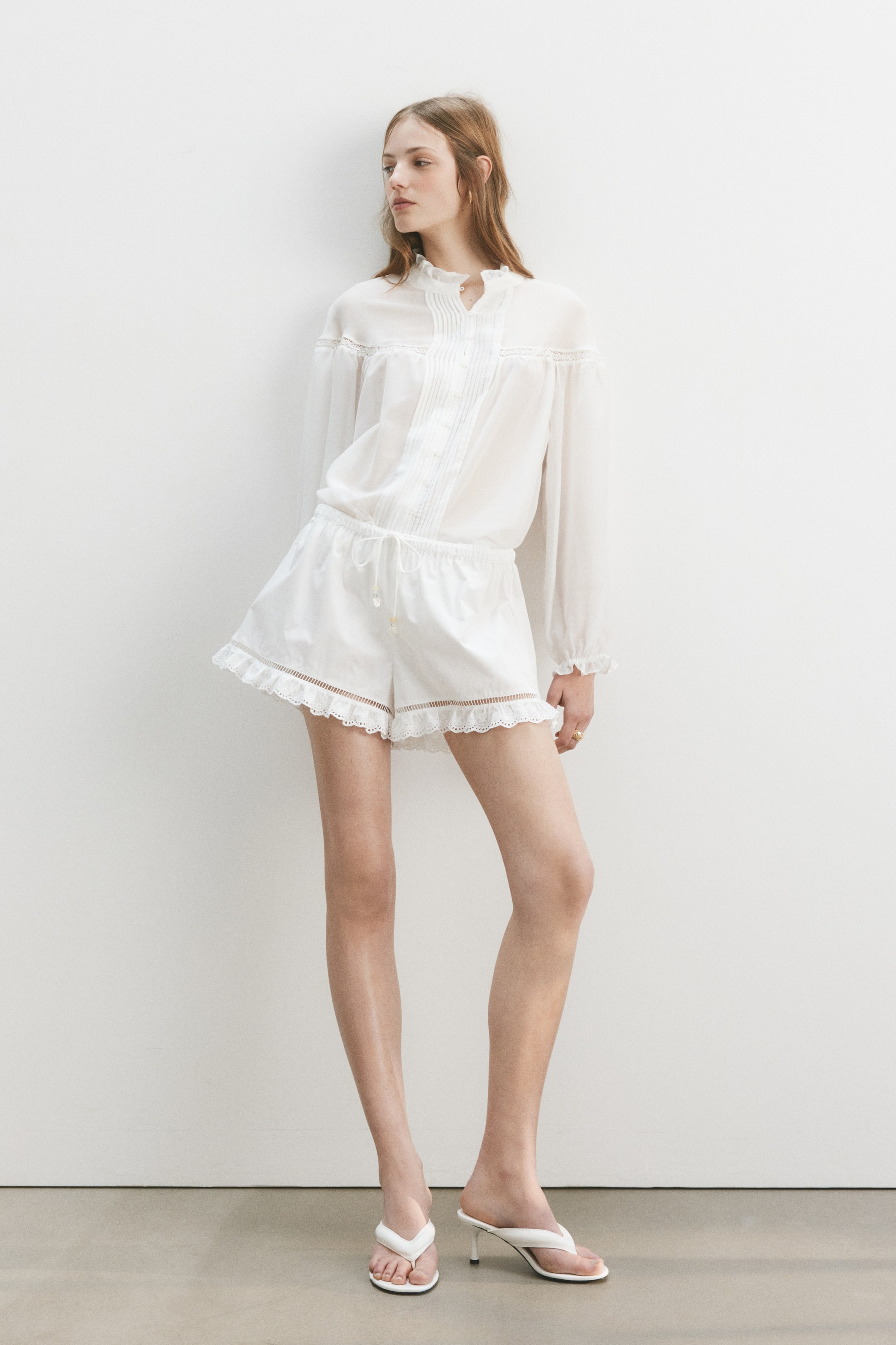 Größeres Bild ansehen: Die Model trägt knackige Baumwoll-Popeline-Shorts mit normaler Taille, die mit einem verdeckten Gummizug und einem gebundenen Spaghetti-Kordelzug mit Perlenenden ausgestattet sind. Feine Leiter-Spitzeinsätze und ein gewellter Spitzenbesatz zieren die Säume.