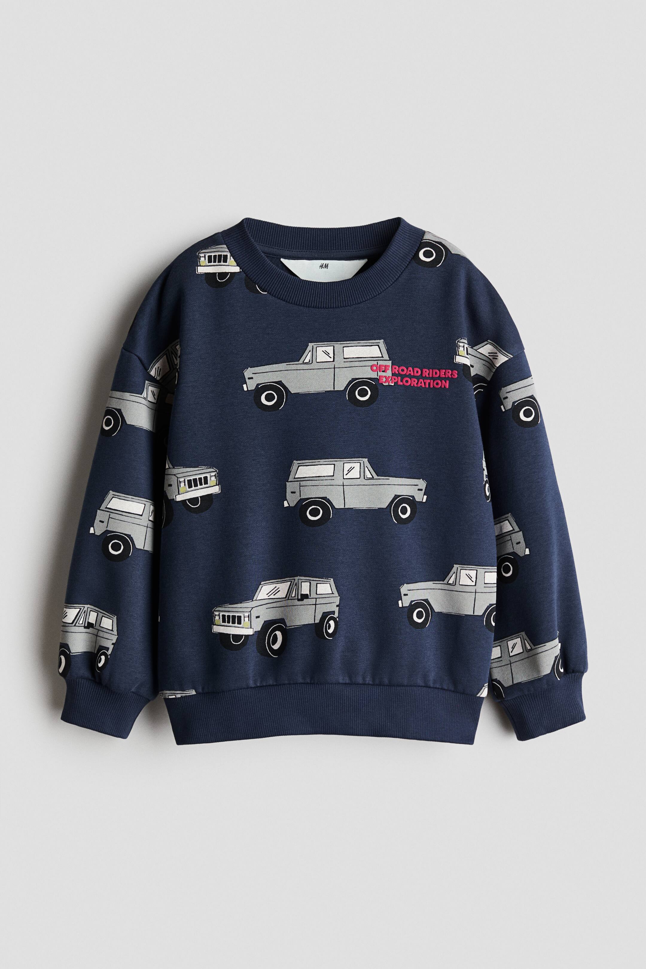 View larger image: A navy blue, loose-fit sweatshirt featuring an all-over print of grey off-road vehicles and pink text reading "OFF ROAD RIDERS EXPLORATION" from a front view. It is designed with a round, ribbed neckline, dropped shoulders, and ribbed trims at the cuffs and hem.