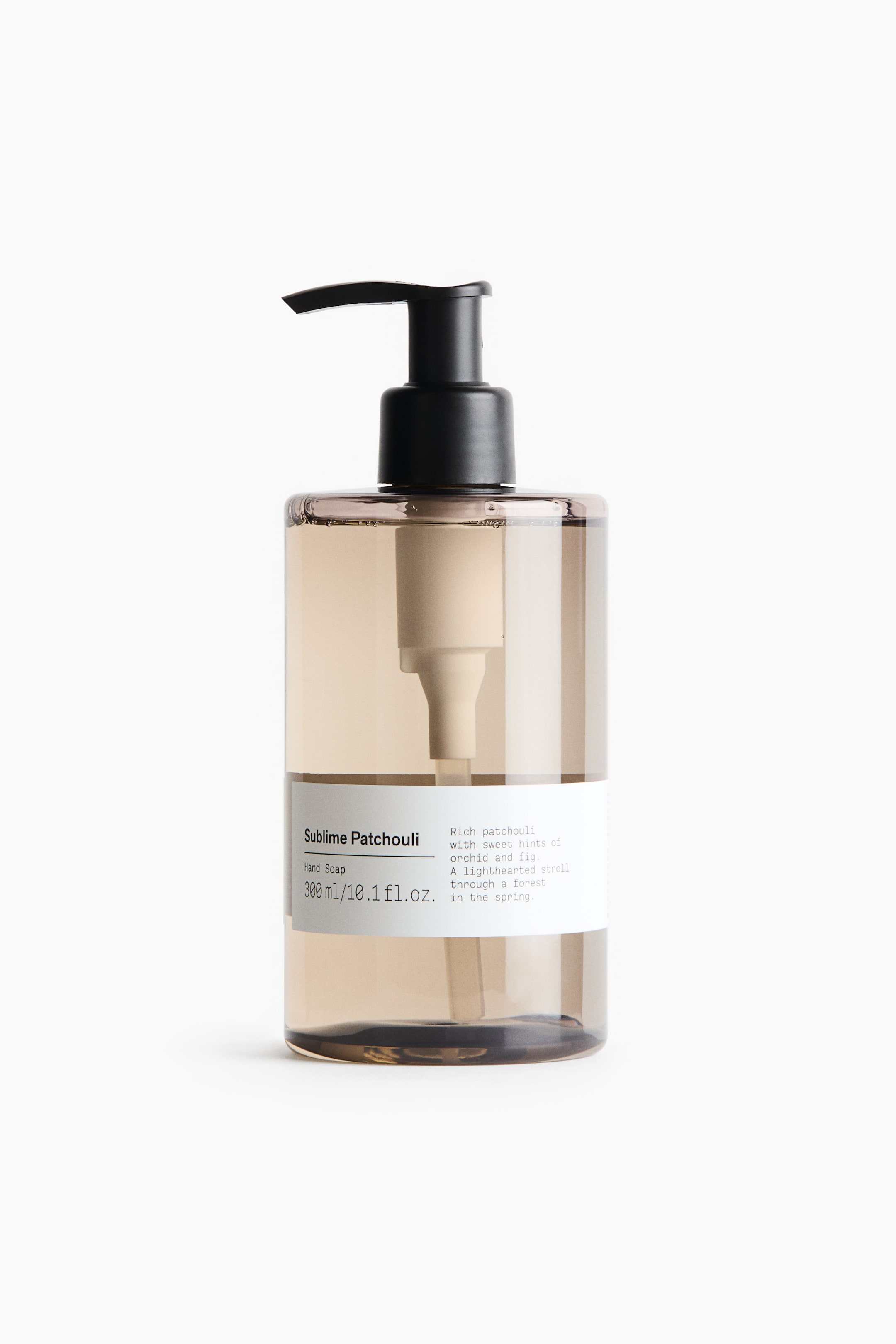 View larger image: A front-facing view of a translucent, amber-tinted cylindrical hand soap bottle featuring a black pump dispenser at the top and filled with a clear, light-brown liquid. A white label wrapped around the lower portion displays black text, with the internal white pump mechanism visible through the container.