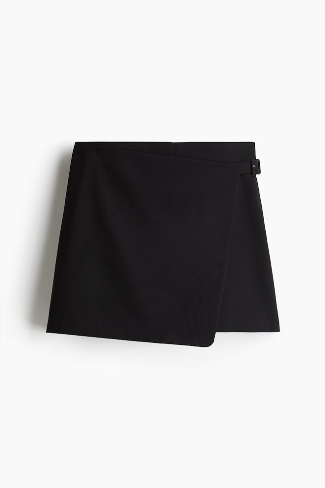 A black skort in woven fabric is presented FRONT, featuring a high waist and a wrapover front with a sewn-in belt that is secured by a covered buckle. - 1