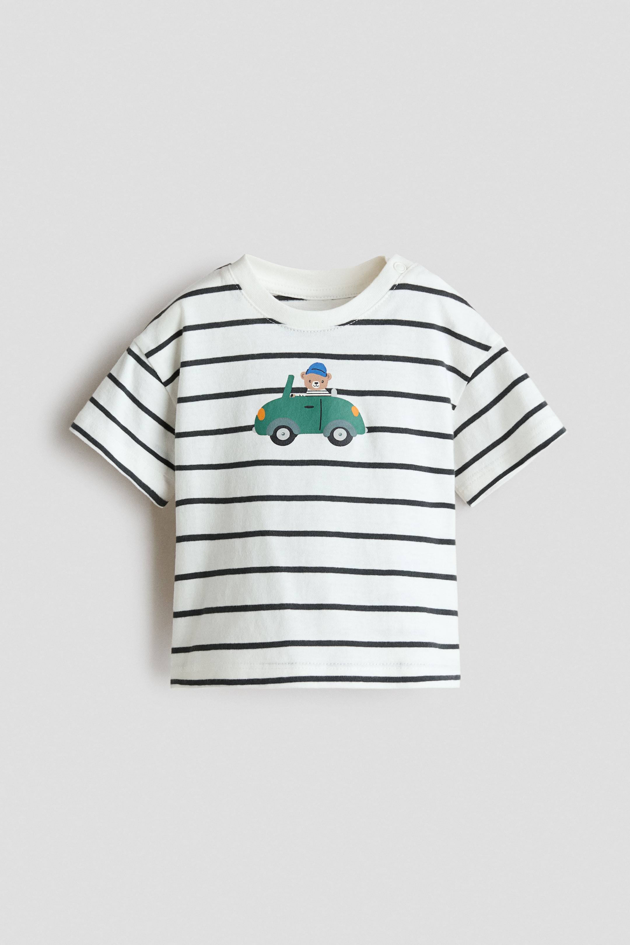View larger image: Printed Cotton T-Shirt. This front-facing tee showcases a white base adorned with horizontal black stripes and short sleeves. The front features a graphic print of a bear wearing a blue hat and driving a green car, complemented by a snap button on the right shoulder.