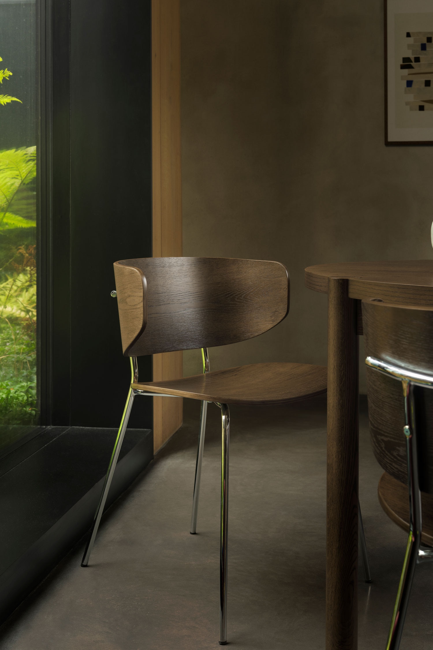Une chaise est orientÃ©e vers lâavant, avec un dossier incurvÃ© en bois brun foncÃ© et une assise profilÃ©e aux veines apparentes. Quatre pieds mÃ©talliques fins, chromÃ©s, soutiennent la chaise en sâÃ©vasant lÃ©gÃ¨rement vers lâextÃ©rieur.