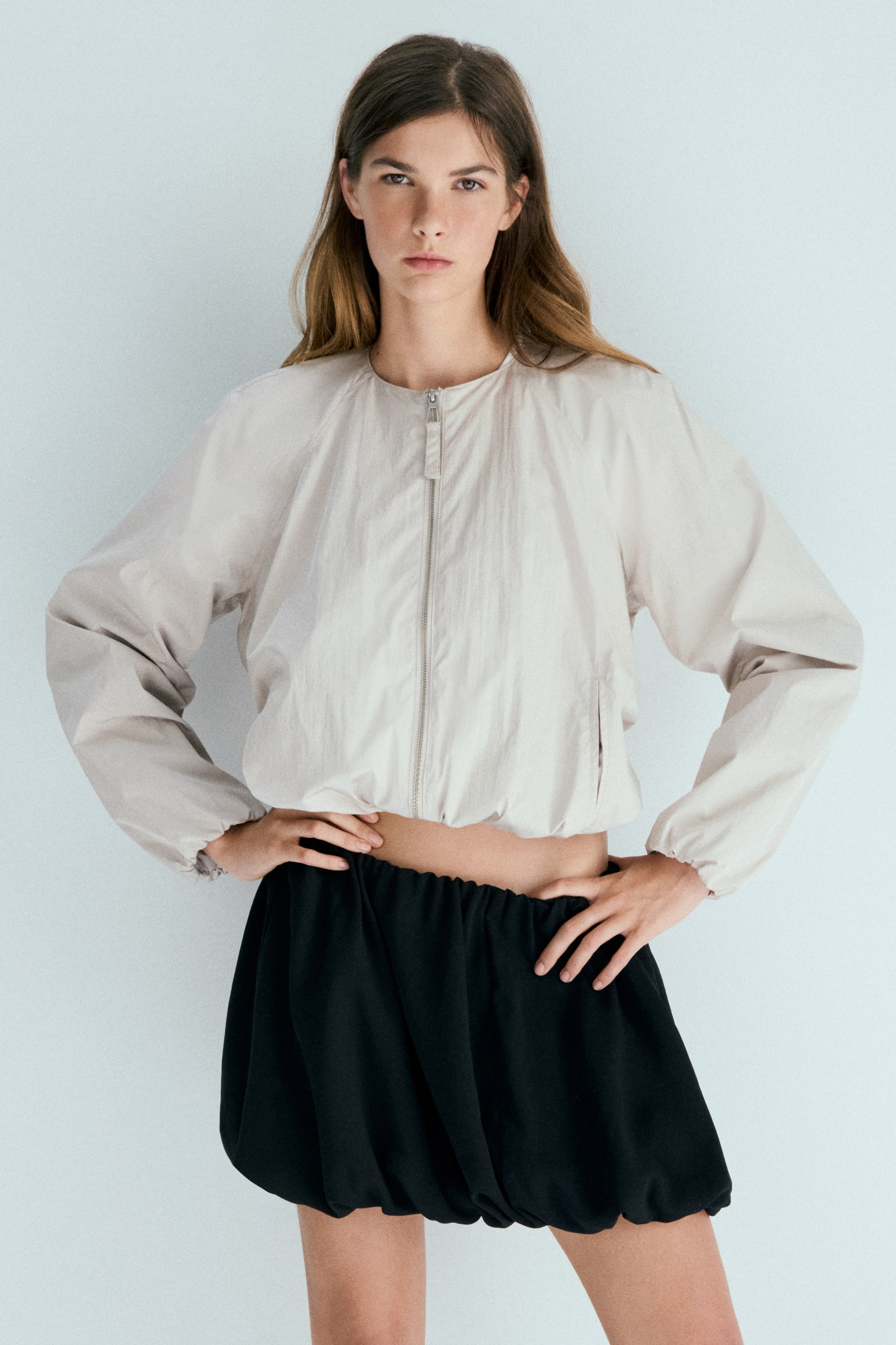View larger image: A light beige cropped bomber jacket featuring a full-zip front closure, a round neckline, and long raglan sleeves with elasticated cuffs and hem, creating a blouson silhouette.