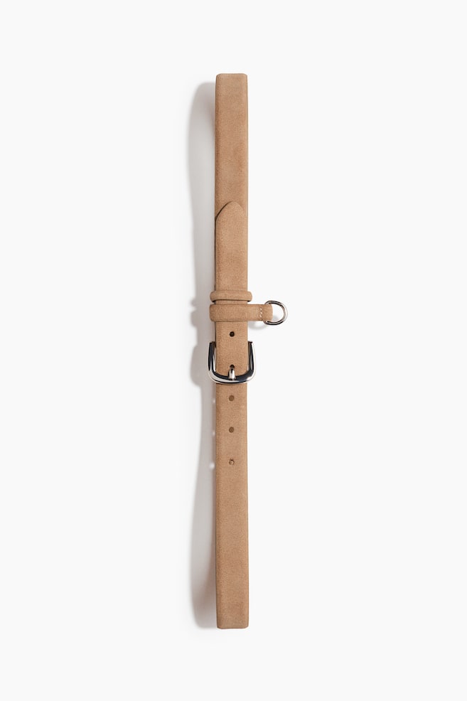 Une ceinture en daim beige est posée à plat et verticalement, avec une boucle à ardillon argentée, deux passants et un anneau en O argenté attaché. - 1
