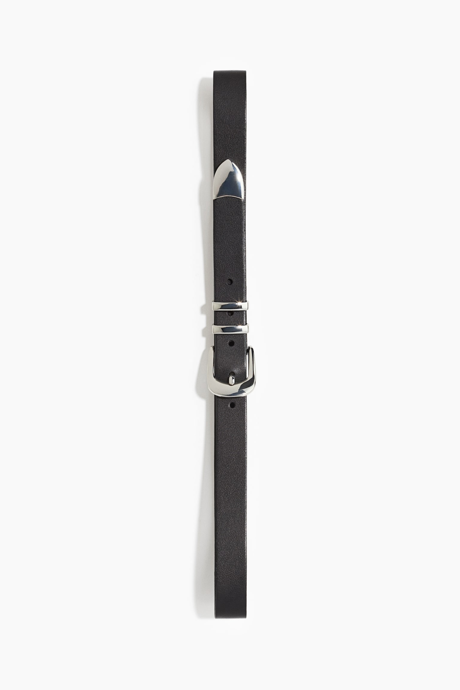 A slim black leather belt is shown vertically, featuring a polished silver-tone Western-style buckle, double metal keepers, and a pointed metal tip. The strap has a smooth matte finish with pre-punched sizing holes.