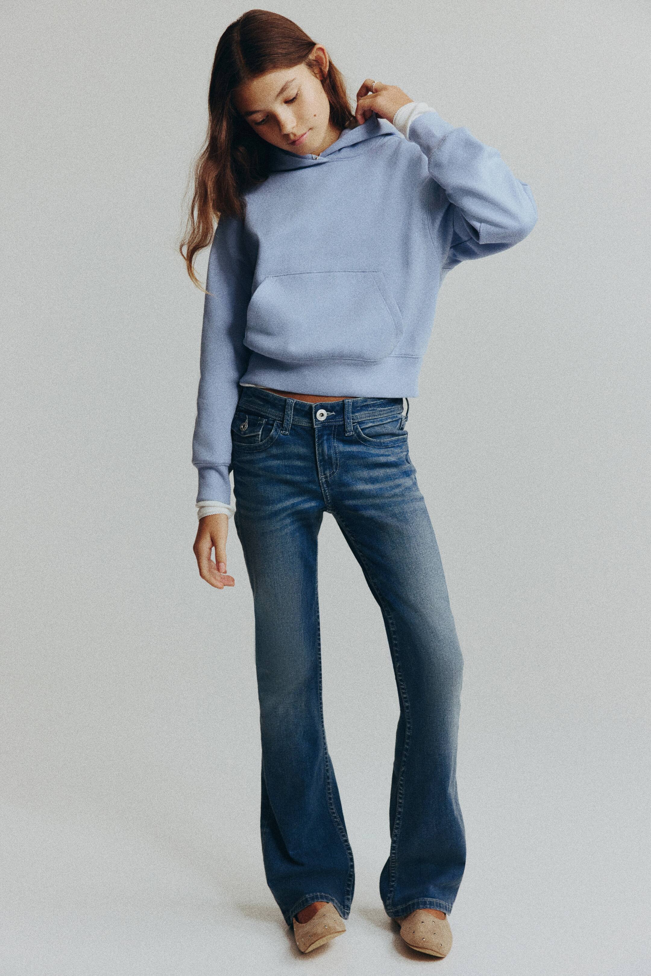 Grotere afbeelding bekijken: Deze jeans met lage taille en vijf zakken, gemaakt van gewassen blauw katoenen denim, worden van voren getoond en hebben een skinny pasvorm ter hoogte van de heupen en dijen, met uitlopende pijpen. De jeans worden gecombineerd met een lichtblauwe hoodie, waardoor de lage taille, de knoopsluiting aan de voorkant en de ritssluiting extra worden benadrukt.
