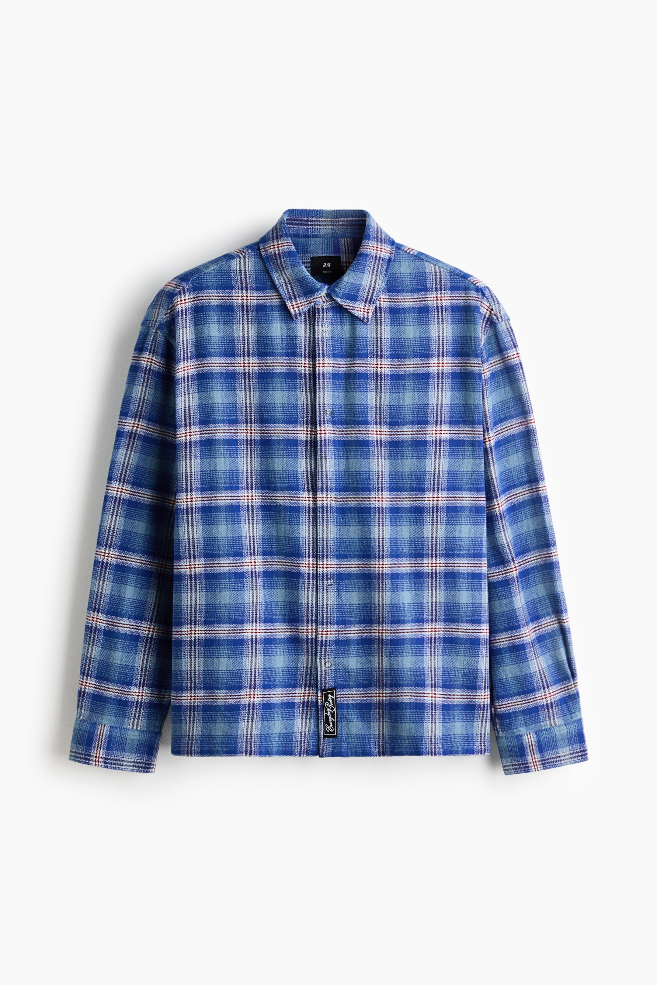 Grotere afbeelding bekijken: Een overhemd met lange mouwen en knoopsluiting toont een blauw-wit geruit patroon met dunne rode strepen, weergegeven vanuit een frontale hoek. Het heeft een klassieke puntkraag, een centrale knoopsluiting, manchetten met knopen en een klein zwart rechthoekig label dat net boven de onderzoom in het midden is gestikt.