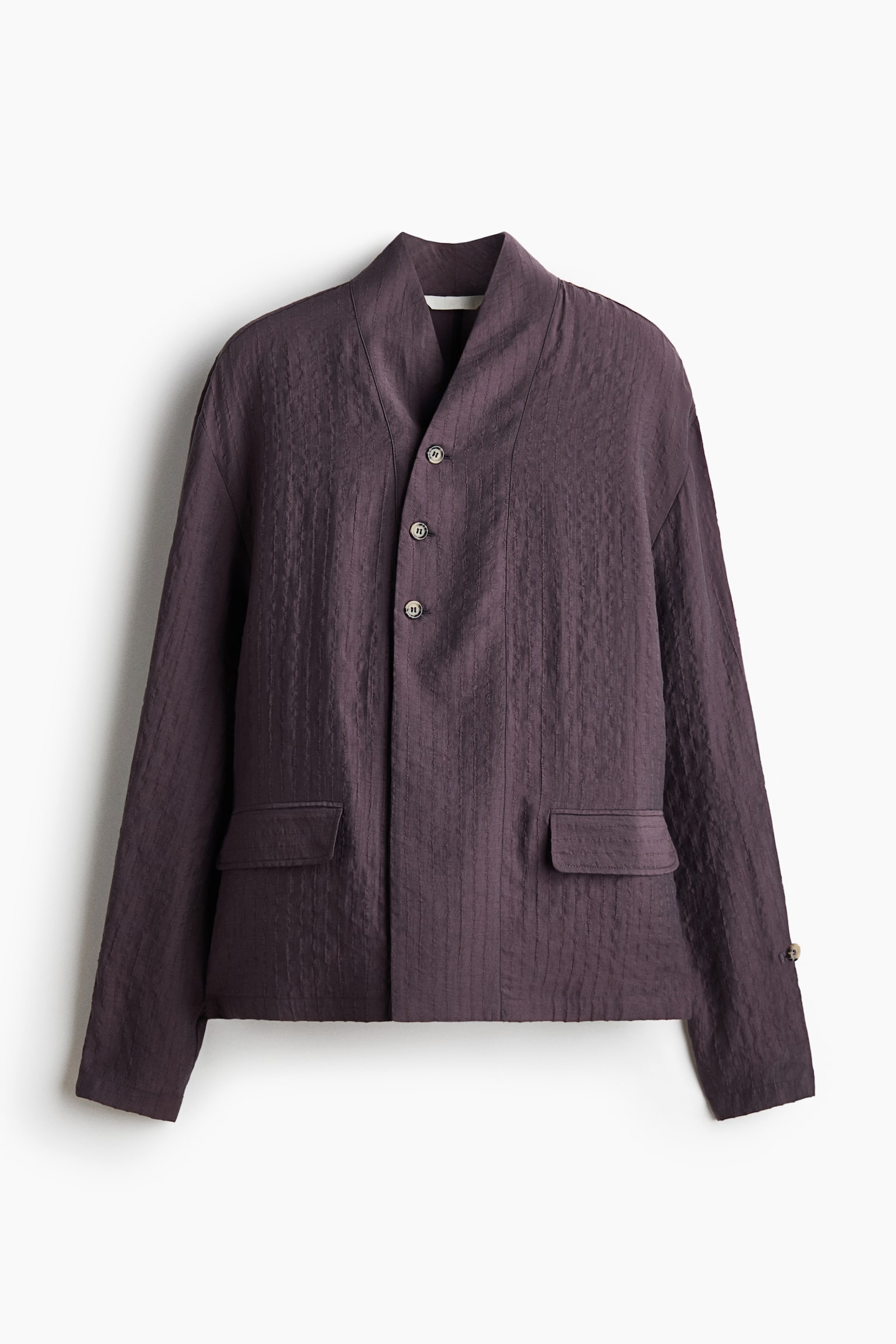Una camicia oversize color prugna scuro, in una trama testurizzata effetto stropicciato, Ã¨ mostrata frontalmente, con colletto alla coreana e chiusura frontale decentrata con tre bottoni nella parte superiore. La camicia presenta spalle scese, maniche lunghe con chiusura a bottone e alamaro vicino al polsino e due tasche frontali con patta sopra un orlo dritto. - 1