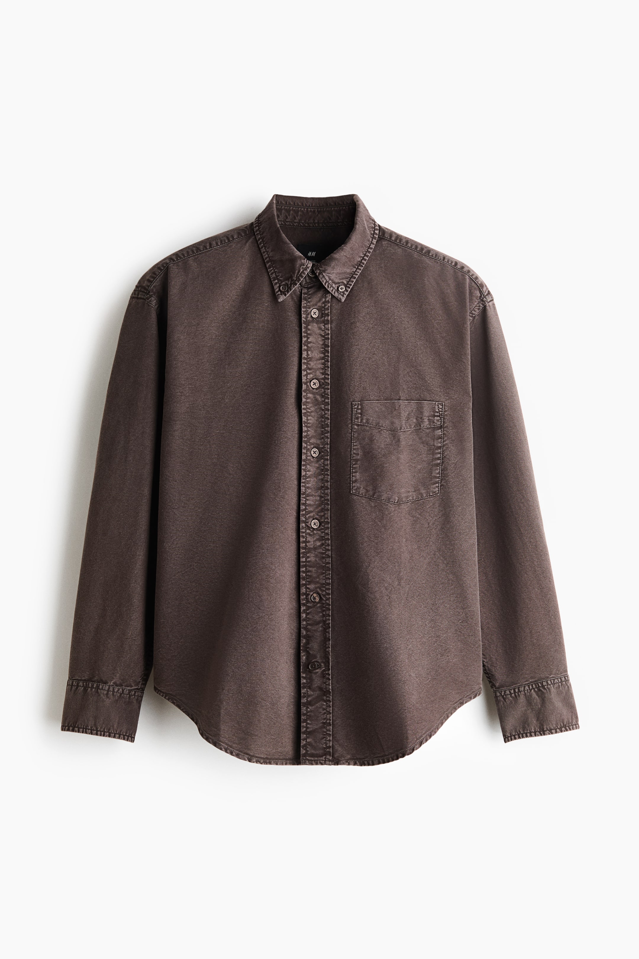 View larger image: A dark brown Oxford cotton shirt is hanging in a front-facing view, displaying a relaxed fit and a button-down collar. It features a classic front button placket, a single open chest pocket, long sleeves with buttoned cuffs, and a gently rounded hem.