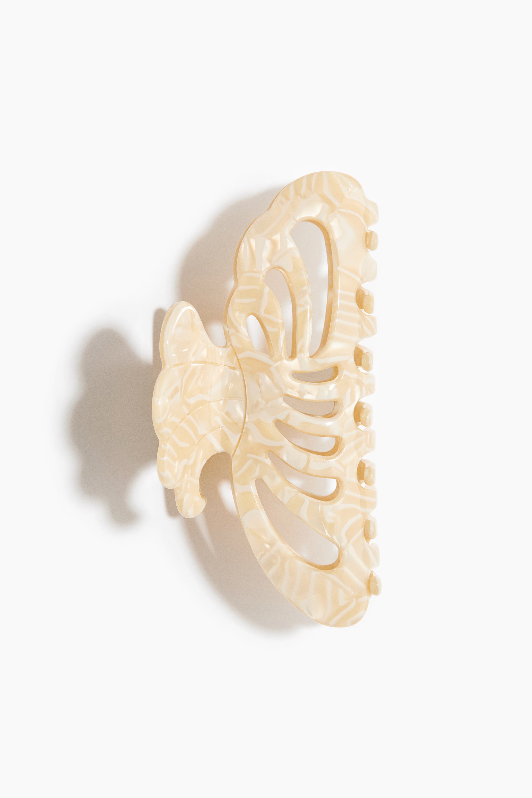 Zobacz większy obraz: Obiekt wykonany z jasnobeżowego acetatu prezentuje przednią stronę z wirującym, marmurkowym wzorem. Z jednej strony ma ozdobny, ażurowy kształt, z drugiej — liczne zęby chwytne.