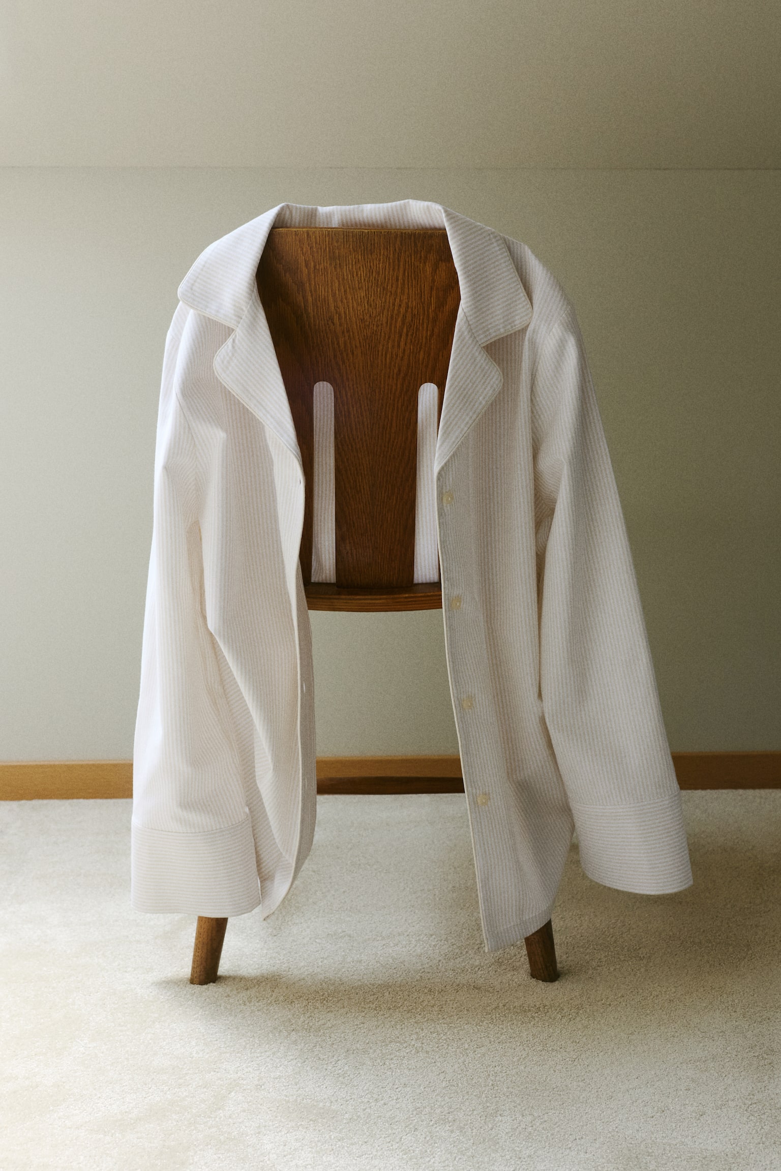 A white pyjama set showcases a long-sleeved button-down top paired with matching wide-leg trousers, both adorned with subtle vertical stripes. The top is crafted with a notch lapel collar and a four-button front closure. - 1
