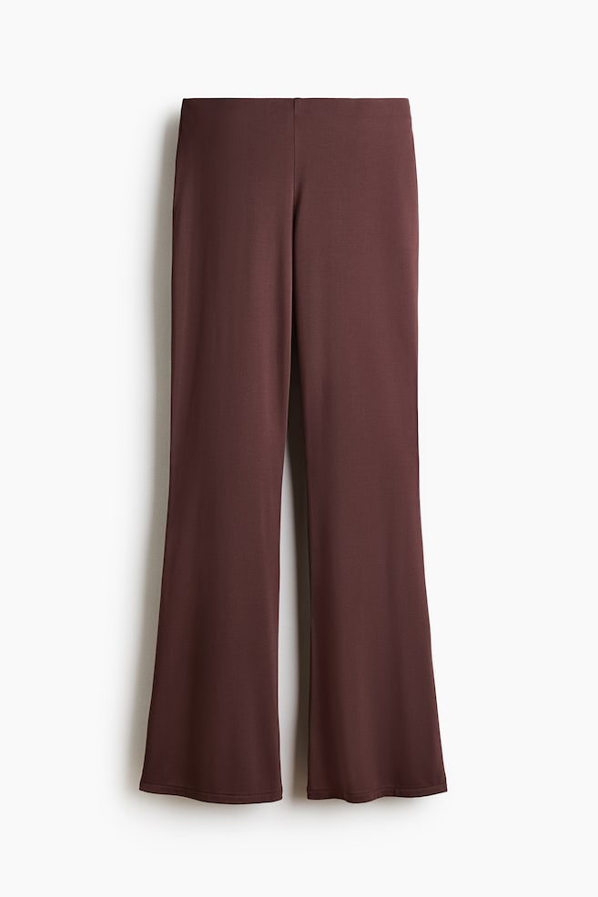 The dark brown trousers feature a smooth fabric and a flat waistband, with legs flaring towards the hem. - 1