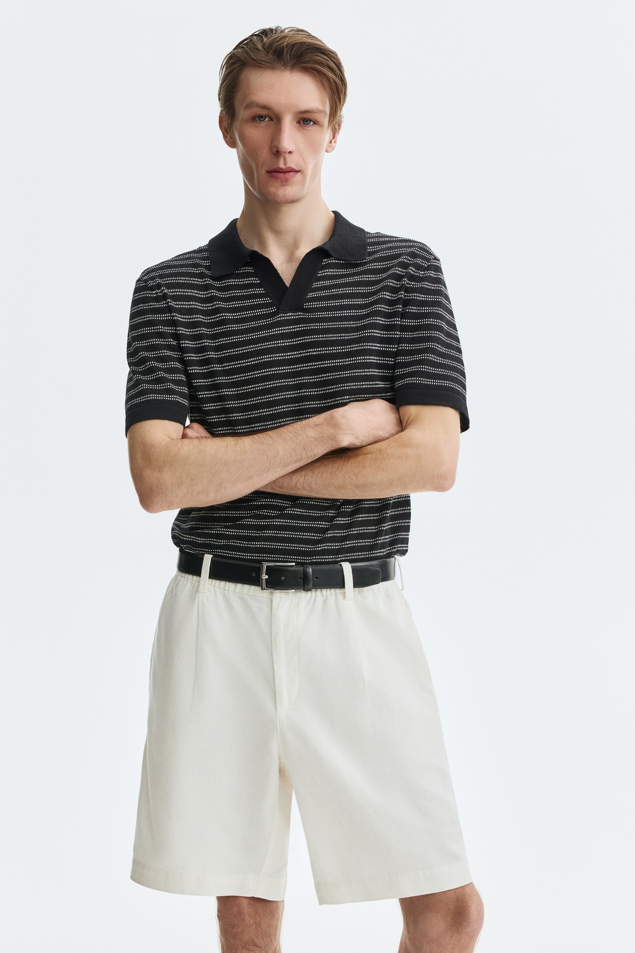 Xem ảnh lớn hơn: Quần short màu kem, có kiểu dáng thoải mái, xếp ly phía trước và túi bên, đang được người mẫu mặc. Quần short có đai lưng và được phối cùng thắt lưng màu đen.