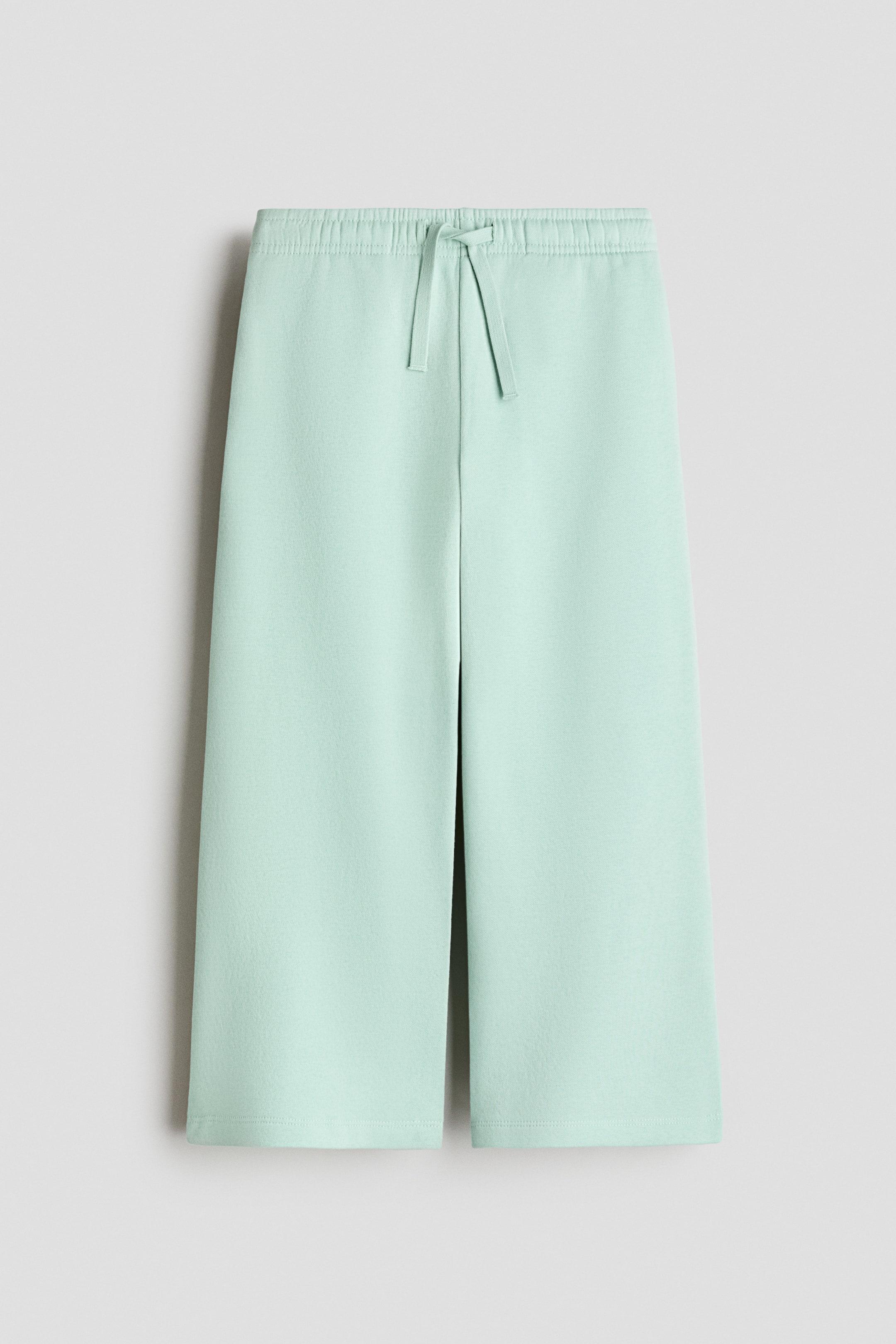 View larger image: Light green fleece track pants are shown from the front, featuring an elastic waistband with a matching drawstring and wide, straight-leg cut.