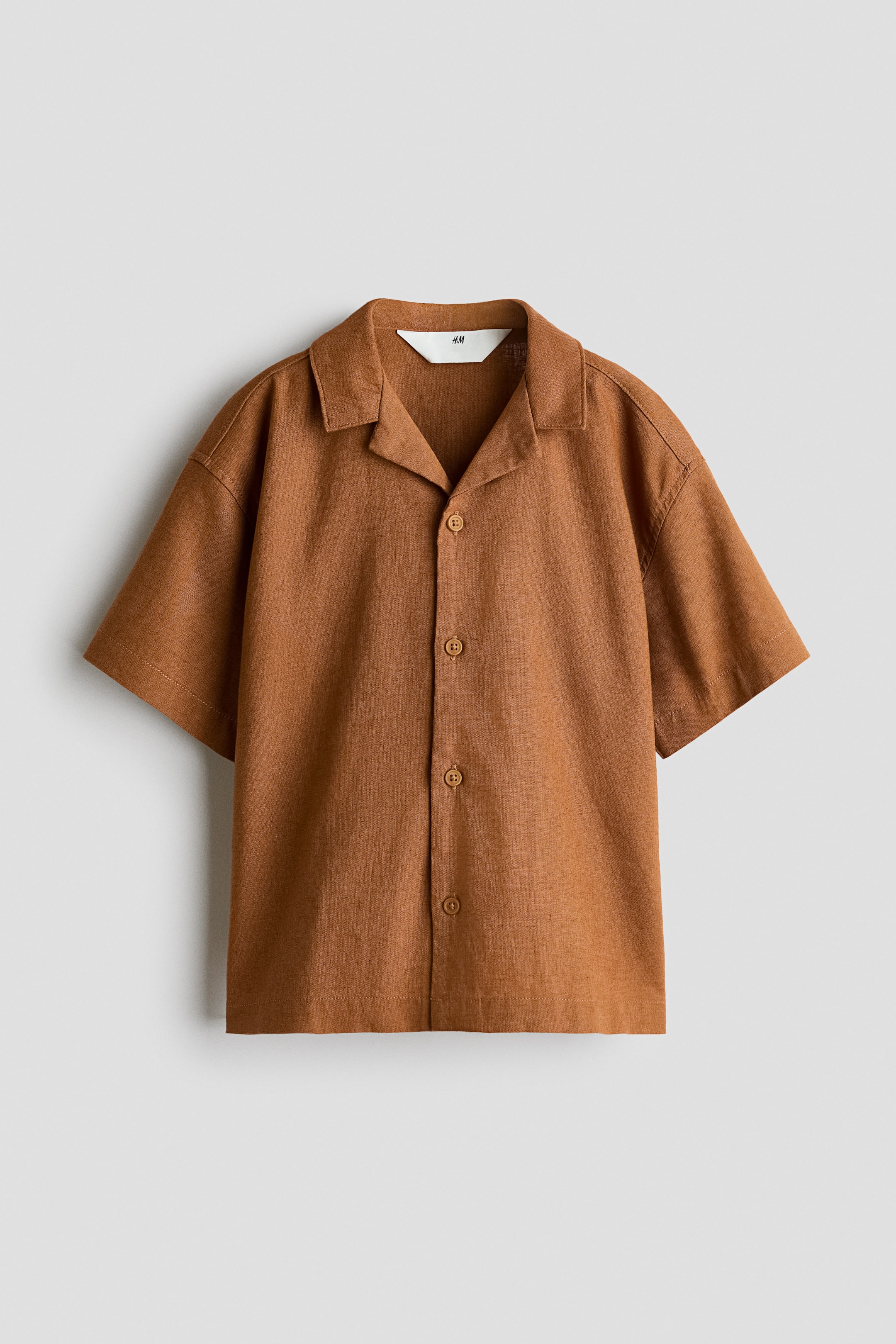 View larger image: A rust-coloured short-sleeved shirt is presenting front-facing, featuring a revere collar and a full button placket with four round buttons. It is made from a textured fabric.