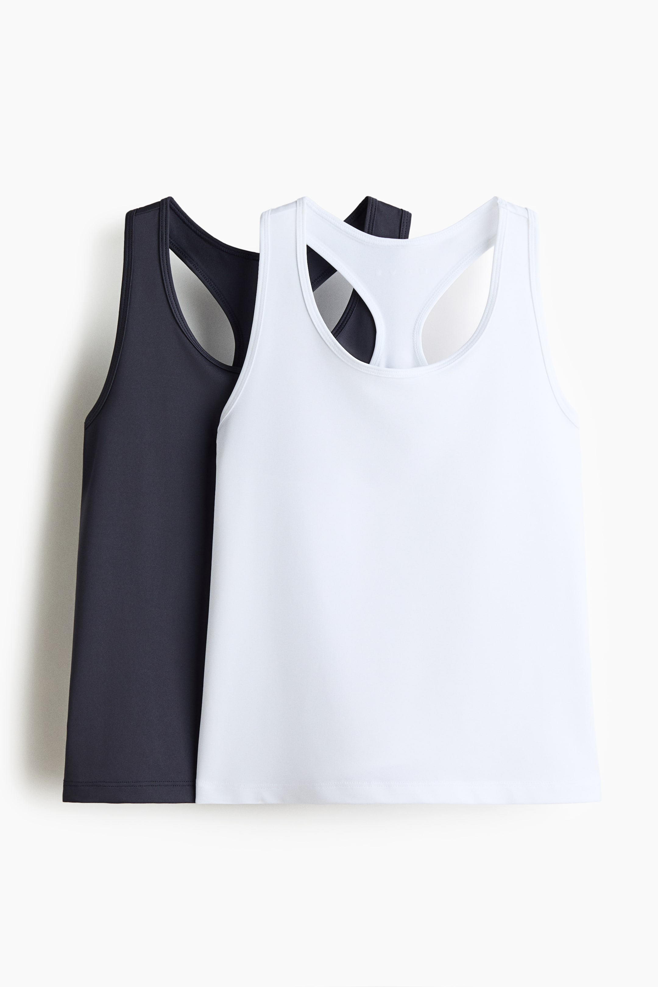 View larger image: Two tank tops are on display, with a white tank top partially overlapping a dark gray tank top. Both tops feature a round neck, wide armholes, and a racerback design.