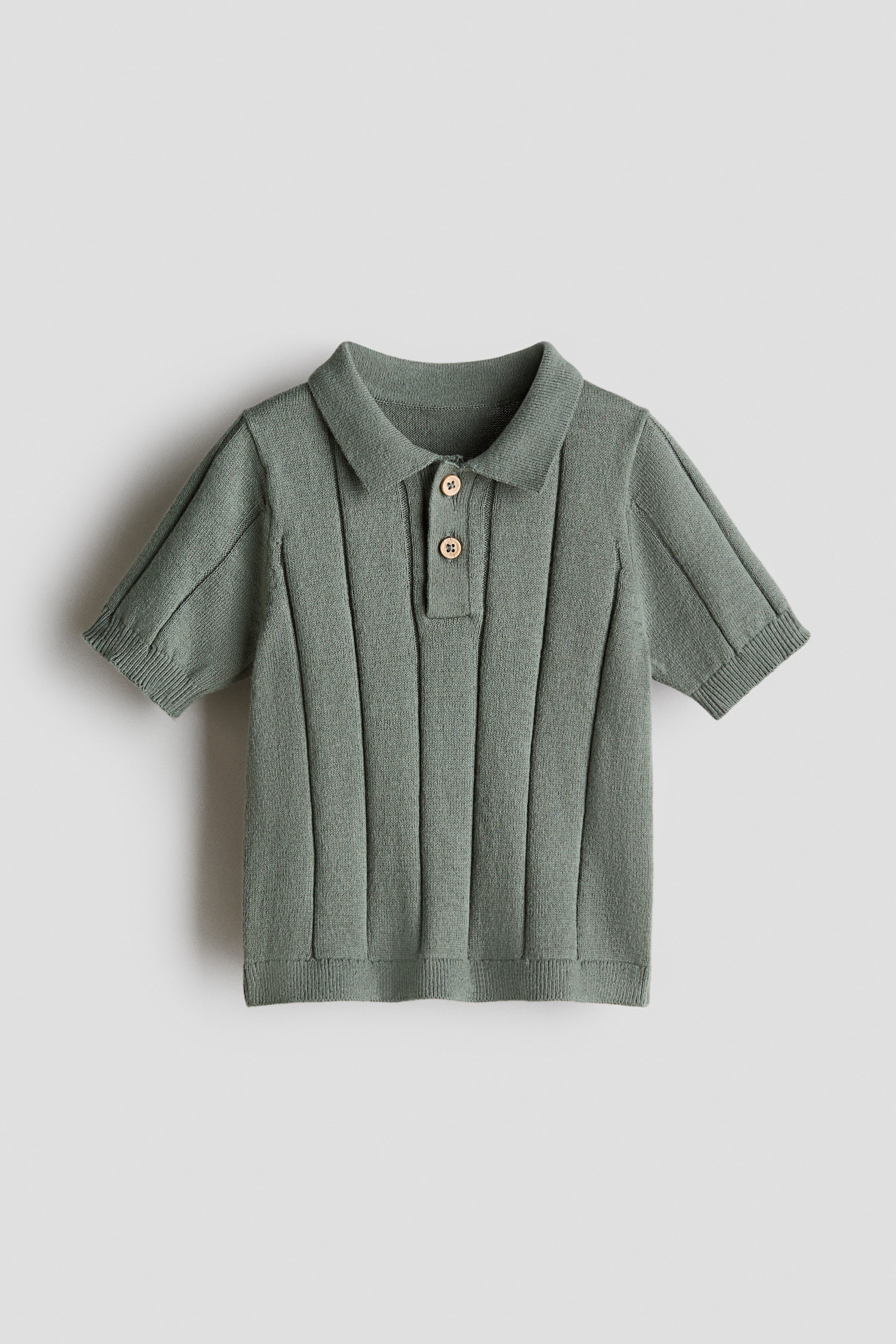 View larger image: A muted green knitted polo shirt is displaying its front view, featuring a collar and a ribbed button band with two light-colored buttons. It is designed with short sleeves, ribbed cuffs, a ribbed hem, and a vertical ribbed texture across the body.