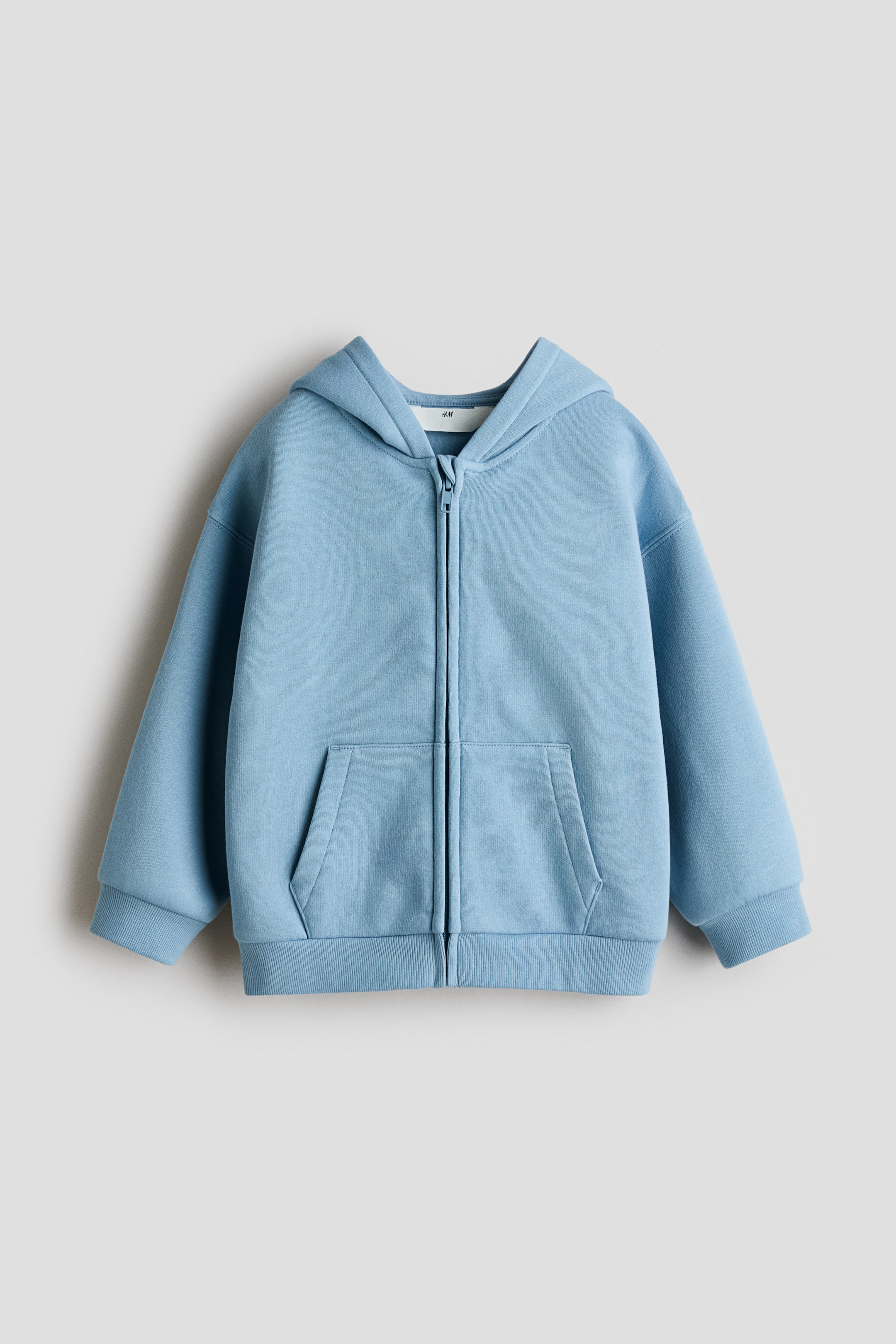 Visualizza immagine più grande: Una felpa con cappuccio color azzurro chiaro, realizzata in un morbido tessuto spazzolato, è mostrata frontalmente, con una zip a tutta lunghezza, un cappuccio attaccato, una grande tasca a marsupio e polsini e orlo a coste.