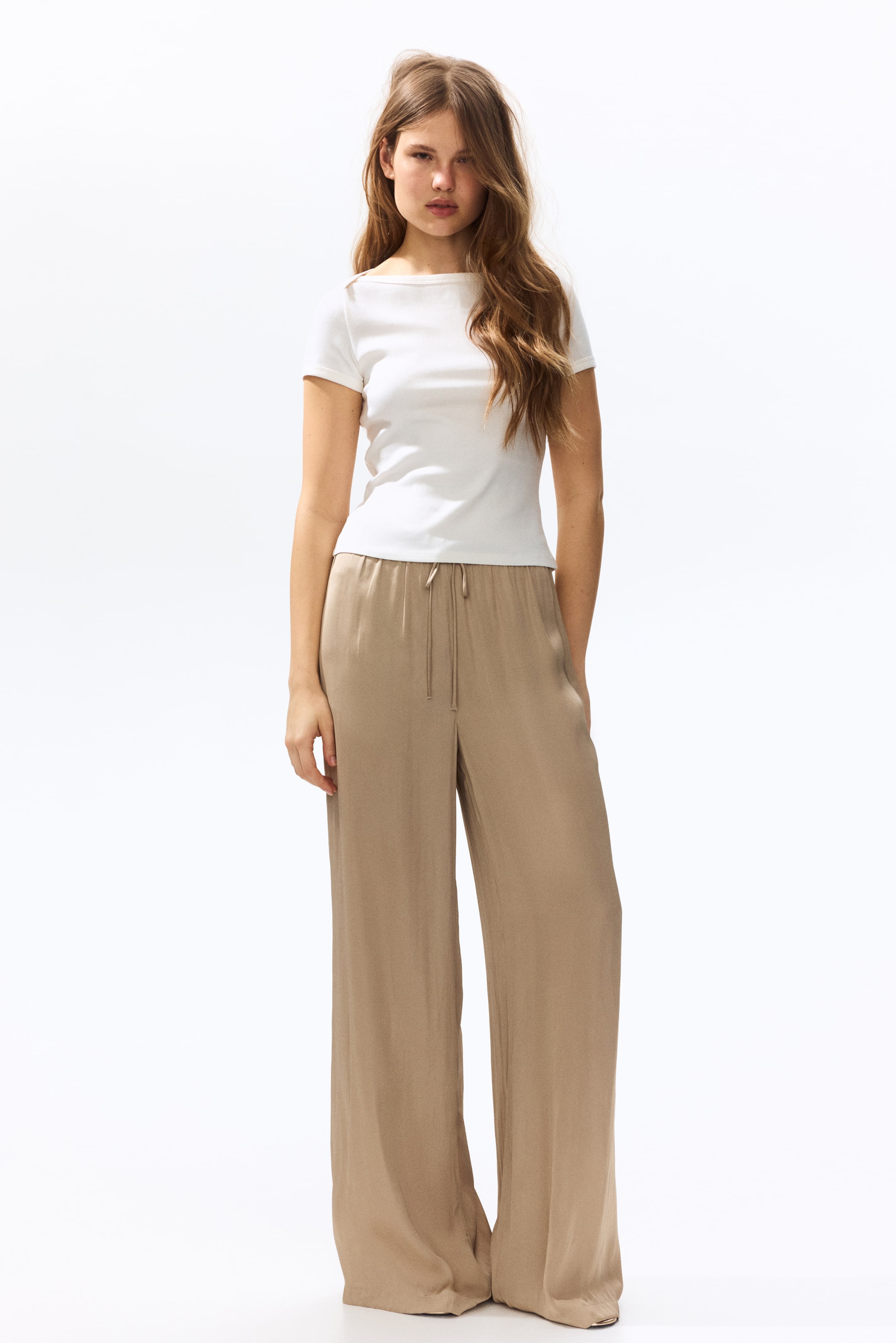 Xem ảnh lớn hơn: Quần ống rộng màu nâu nhạt có dây rút ở eo và túi bên hông, với chất liệu vải mềm mại rủ xuống sàn.