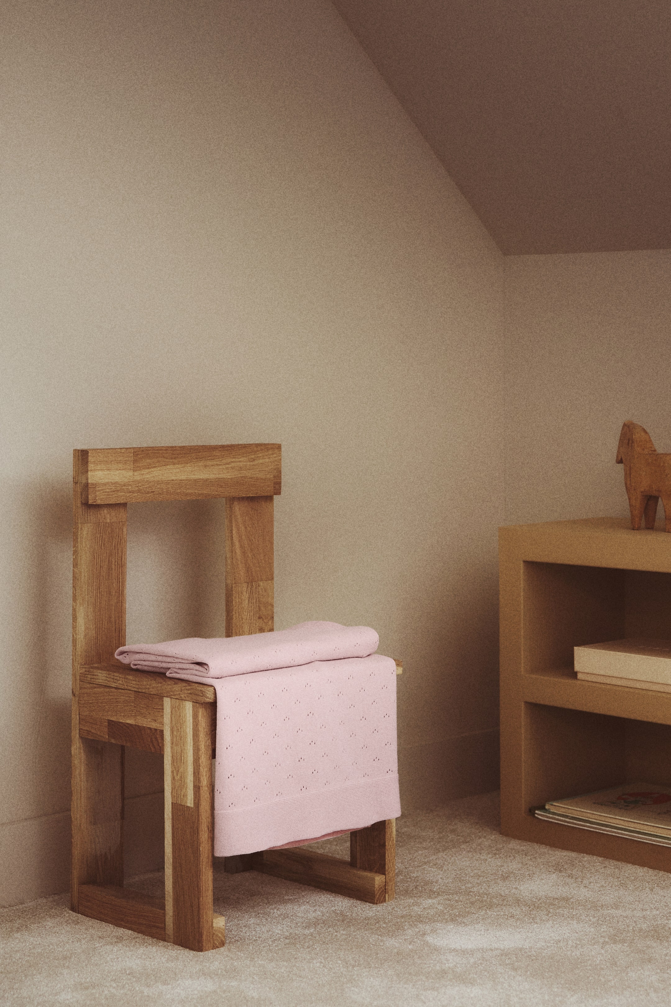 Voir une image plus grande: Une couverture pour bébé douillette, confectionnée en tricot pointelle de coton rose doux, est pliée et drapée sur une chaise. Elle présente un motif délicat de petits œillets sur toute sa surface et des bordures tricotées solides aux extrémités.