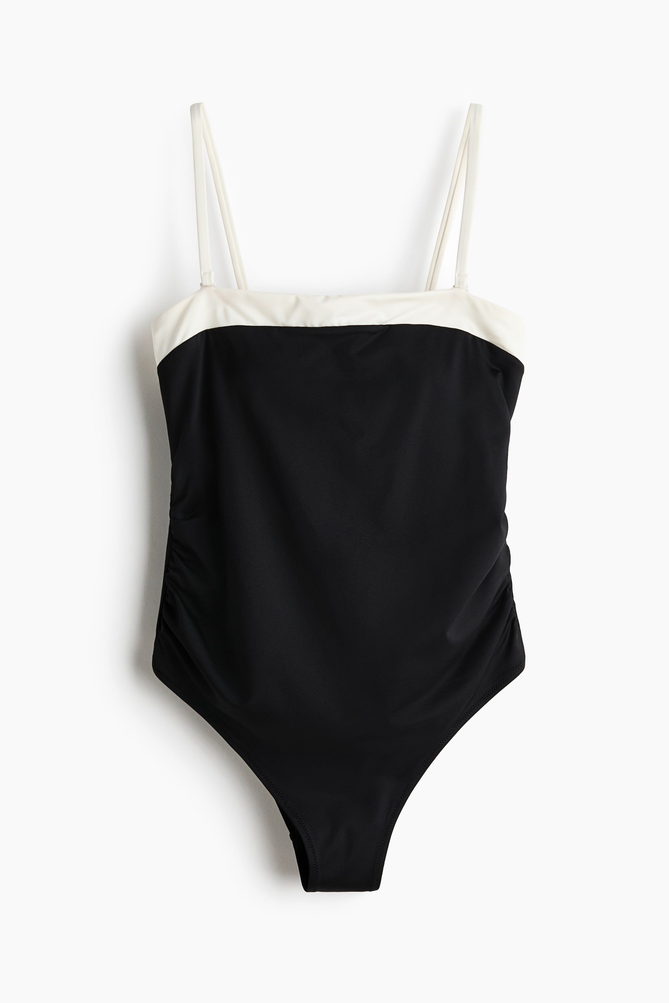View larger image: A swimsuit is presenting FRONT, featuring a black body with a contrasting white band across the strapless top. Thin white spaghetti straps are extending from the top, and subtle ruching is detailing both sides of the black body.
