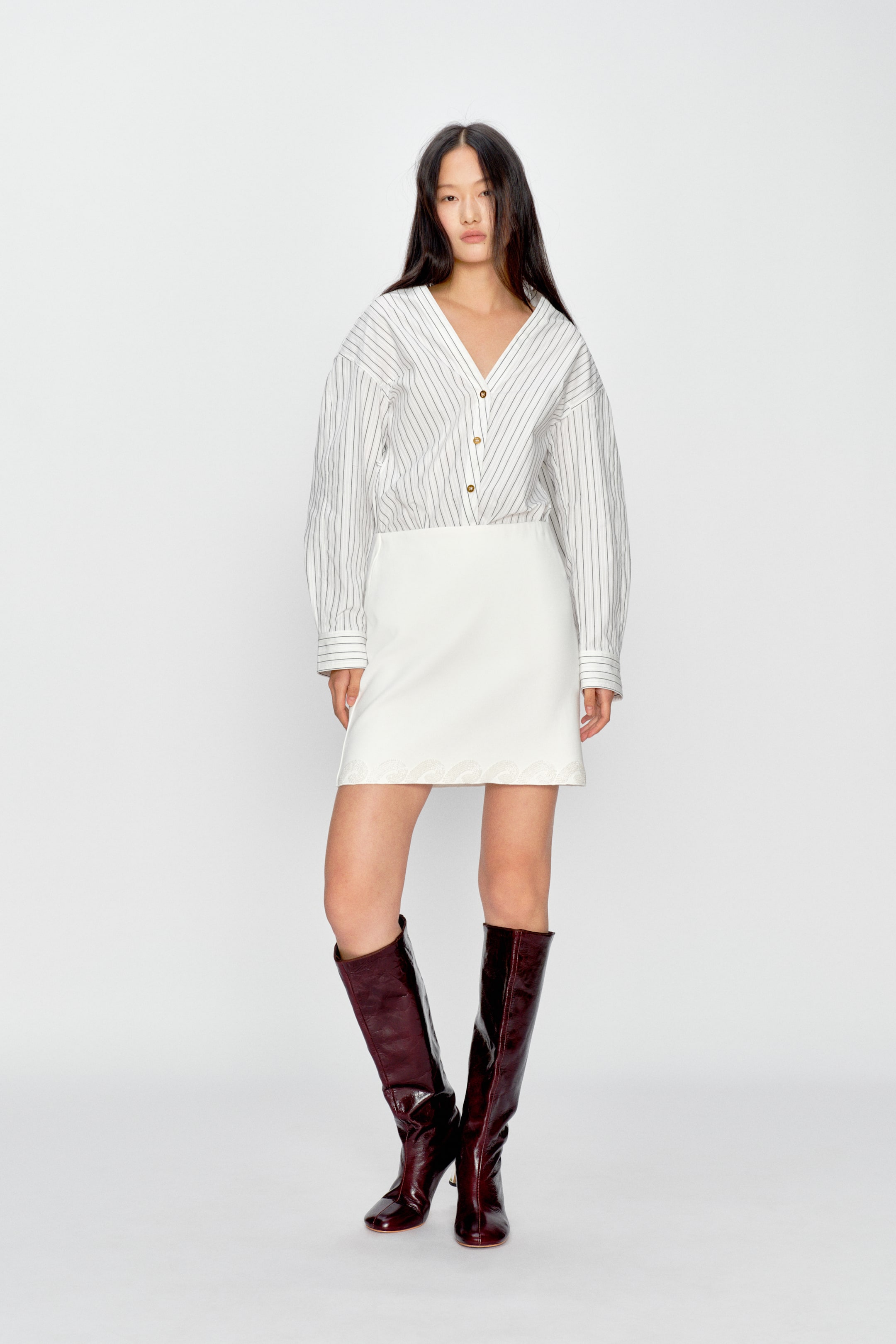 View larger image: A white mini skirt is shown from the front, featuring a straight cut and a high-waisted design. The hemline is finished with a subtle scalloped detail.