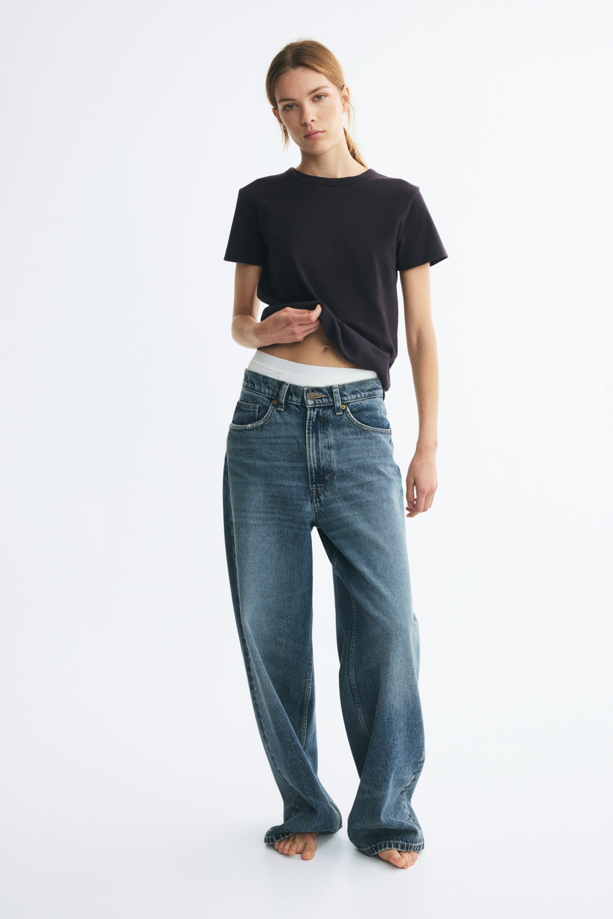 A dark fitted t-shirt in heavy cotton jersey is lying flat, showcasing short sleeves, ribbing around the neckline, and a straight-cut hem.