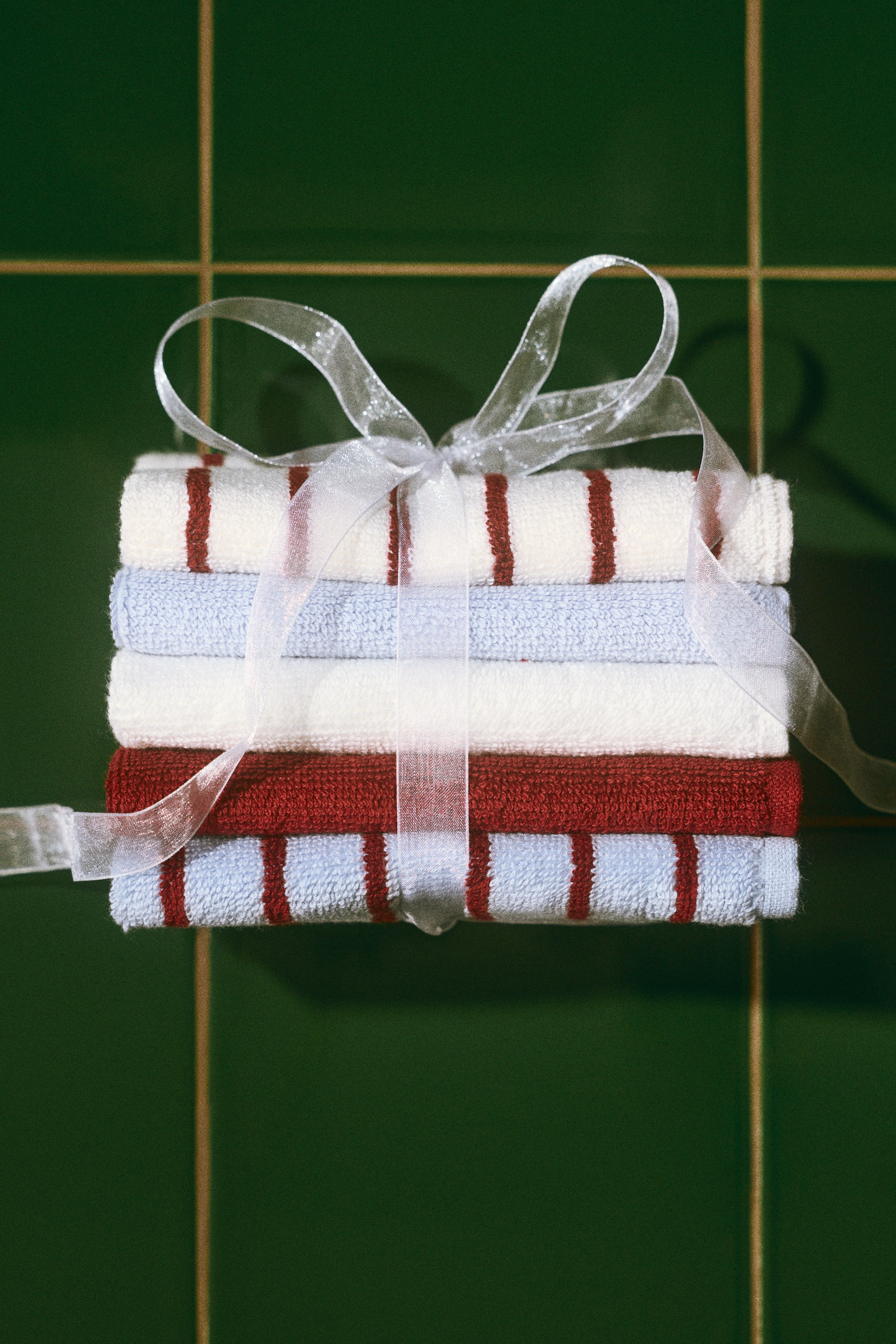 View larger image: A set of five cotton terry face cloths is stacked vertically from a front view, tied together with a sheer white ribbon bow. The collection features solid and striped designs in white, light blue, and dark red.