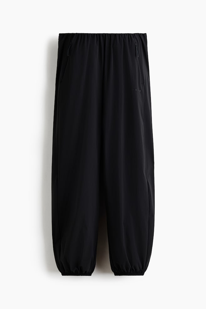 Se muestra un par de pantalones negros de frente, con pretina elÃ¡stica fruncida y puÃ±os elasticados a juego en el dobladillo. El diseÃ±o de pierna ancha y ajuste relajado presenta discretas bolsas laterales con cierre y una confecciÃ³n en tela ligera y suave. - 1