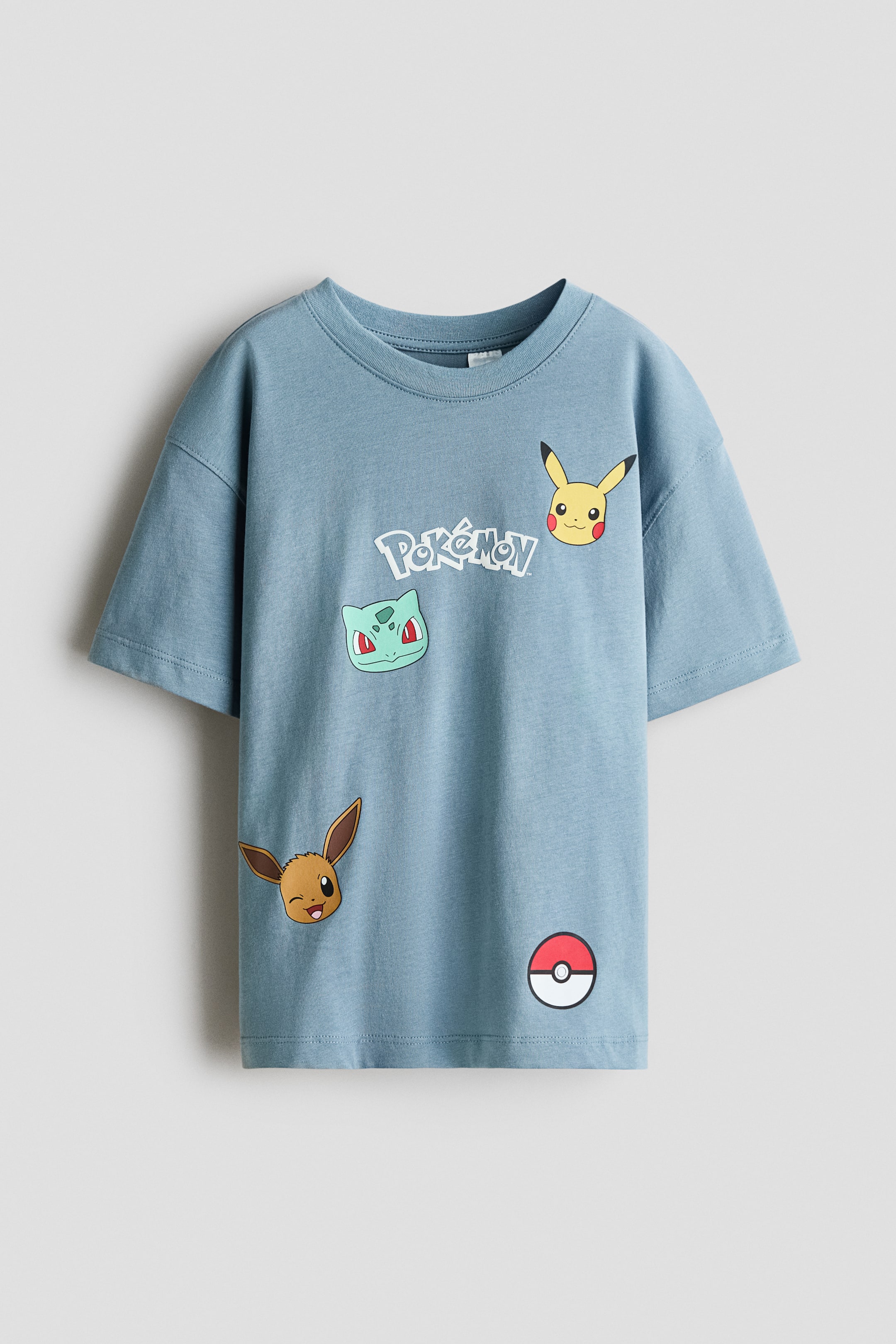 Grotere afbeelding bekijken: Een oversized T-shirt, gemaakt van zachte, blauwe katoenen jersey, met een print op de voorkant van verschillende Pok�mon-personages, waaronder Pikachu, Bulbasaur, Eevee en een Pok� Ball, samen met het 'Pok�mon'-logo. Het is ontworpen met een geribde afwerking aan de halslijn en verlaagde schouders.