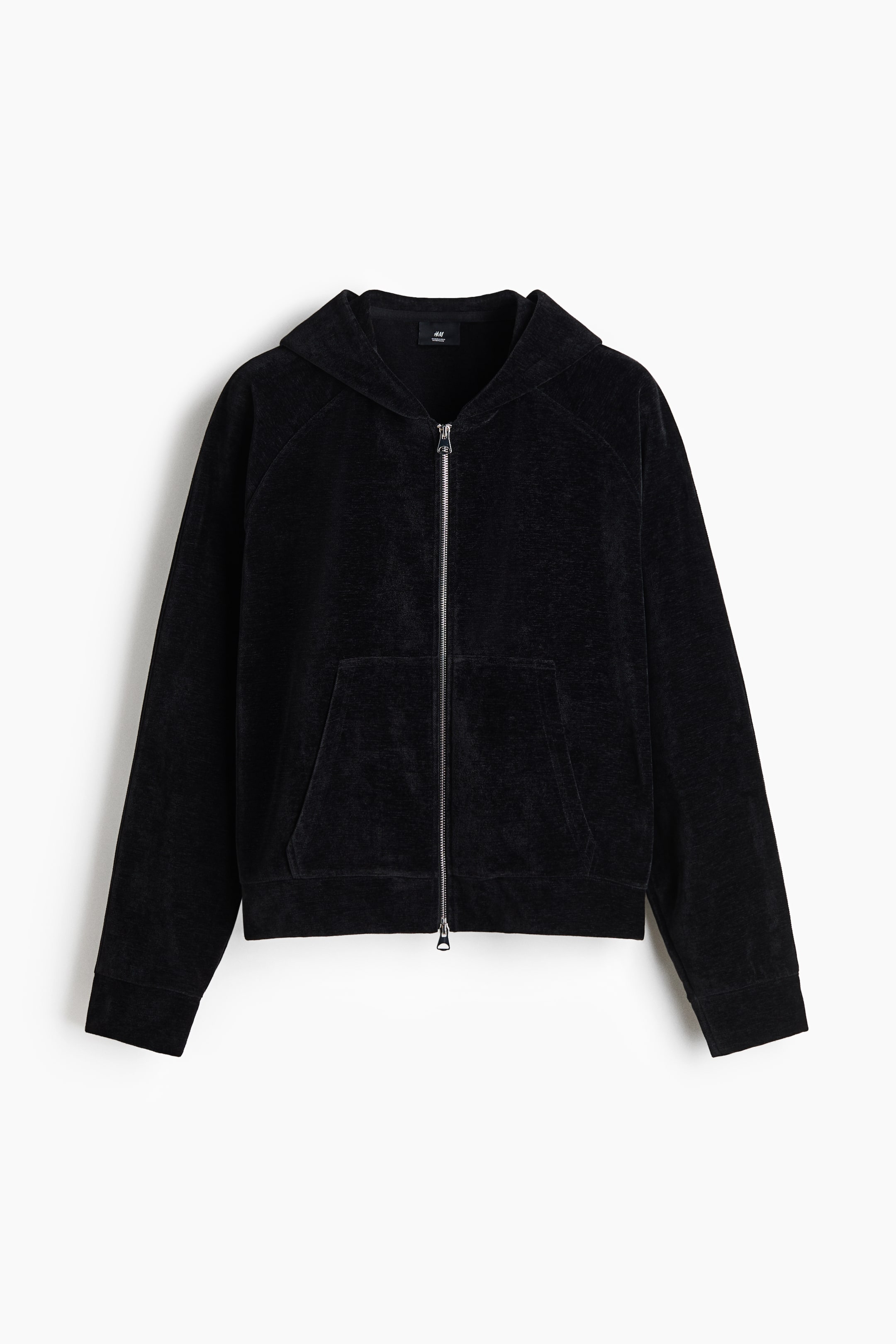 View larger image: A black velour zip-up hoodie is shown from the front, featuring a full-length silver metal zipper, an attached hood, and a split kangaroo pocket. The garment has long raglan sleeves with ribbed cuffs and a matching ribbed hem.